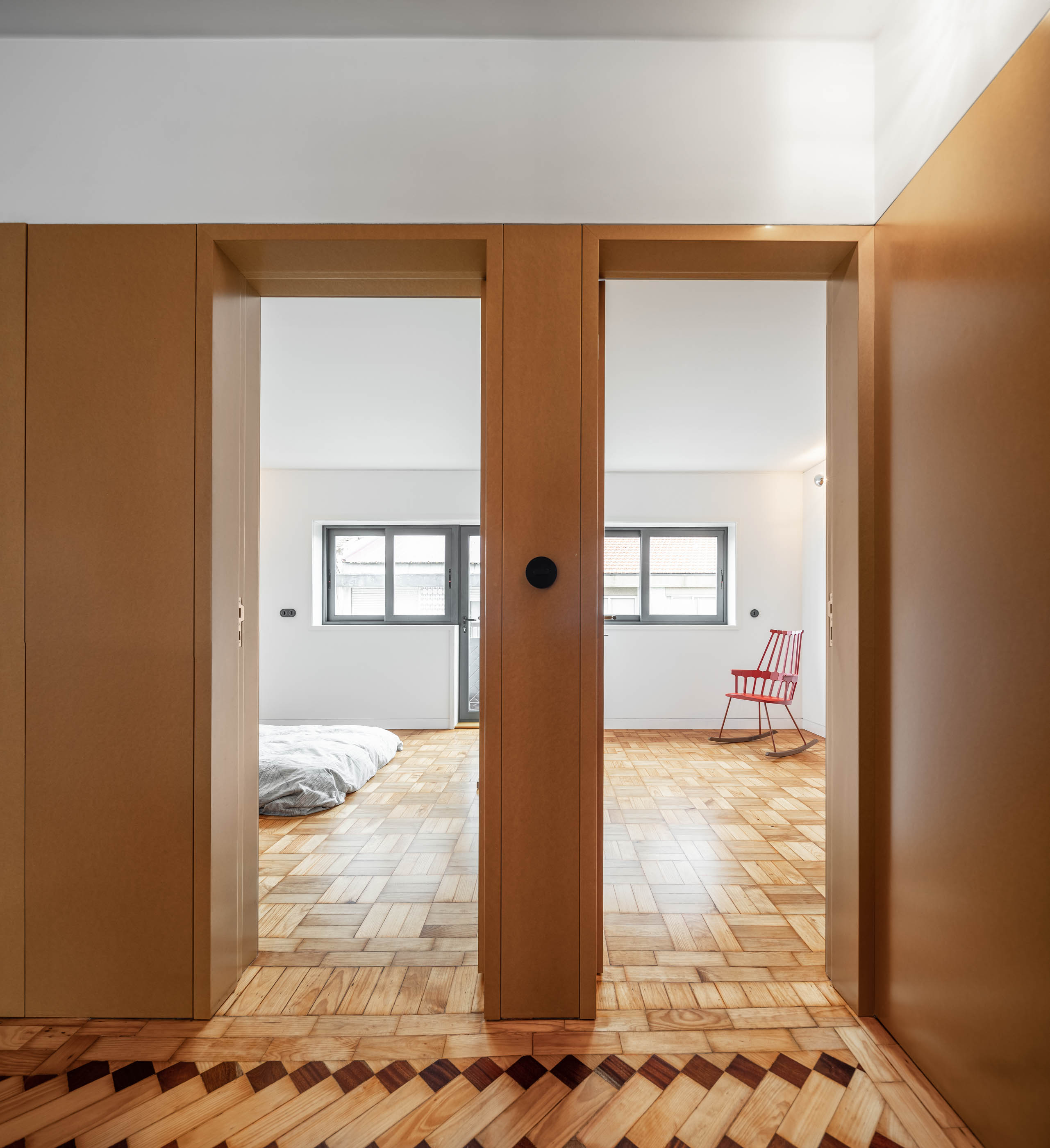 Portas duplas em madeira cor de mel para quartos, com pavimento em madeira com padrão geométrico. — Apartamento Morro arquitetura Hinterland Architecture Studio em Vila Nova de Gaia