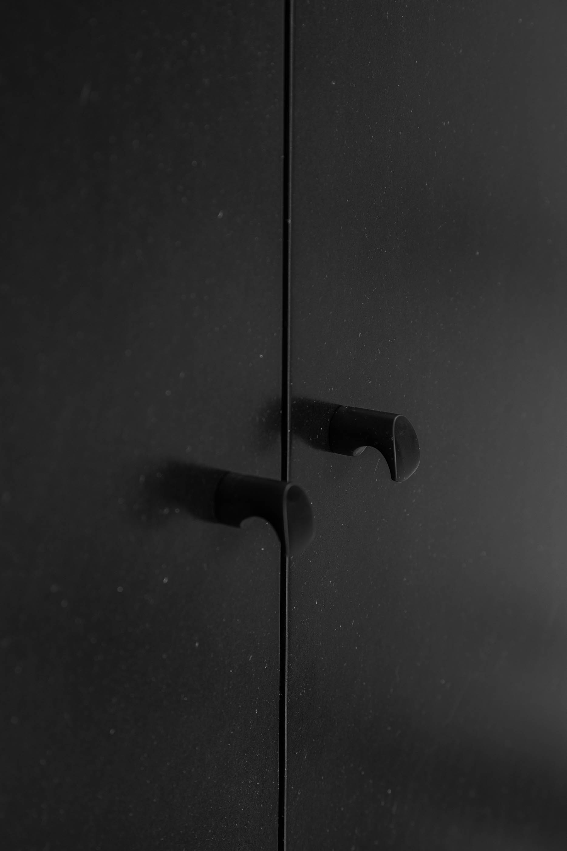 Detalhe de puxadores cilíndricos pretos num armário de linhas minimalistas. — Apartamento Morro arquitetura Hinterland Architecture Studio em Vila Nova de Gaia