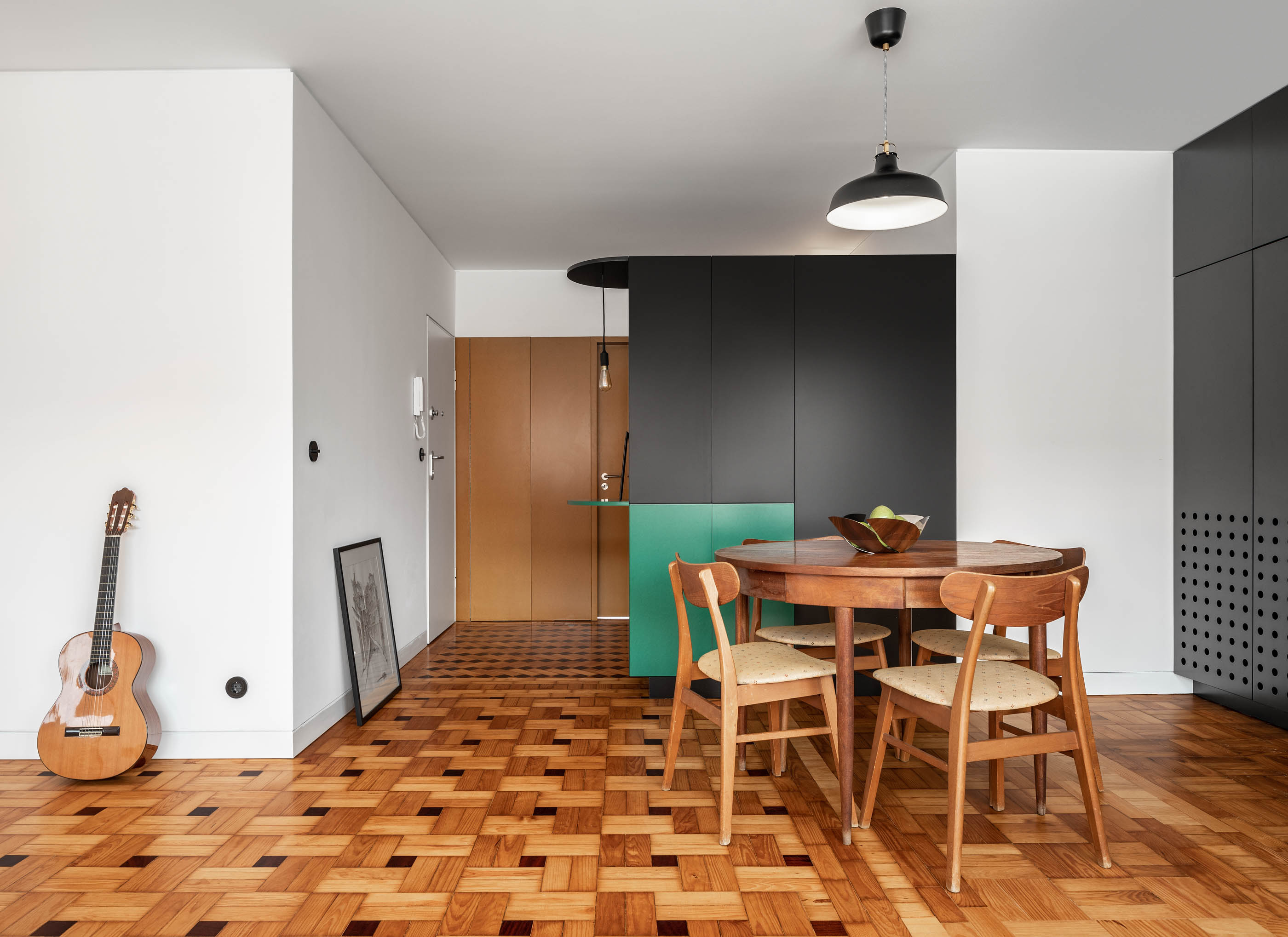 Sala de jantar com mesa redonda, cadeiras de madeira, armário preto e verde e pavimento em madeira. — Apartamento Morro arquitetura Hinterland Architecture Studio em Vila Nova de Gaia