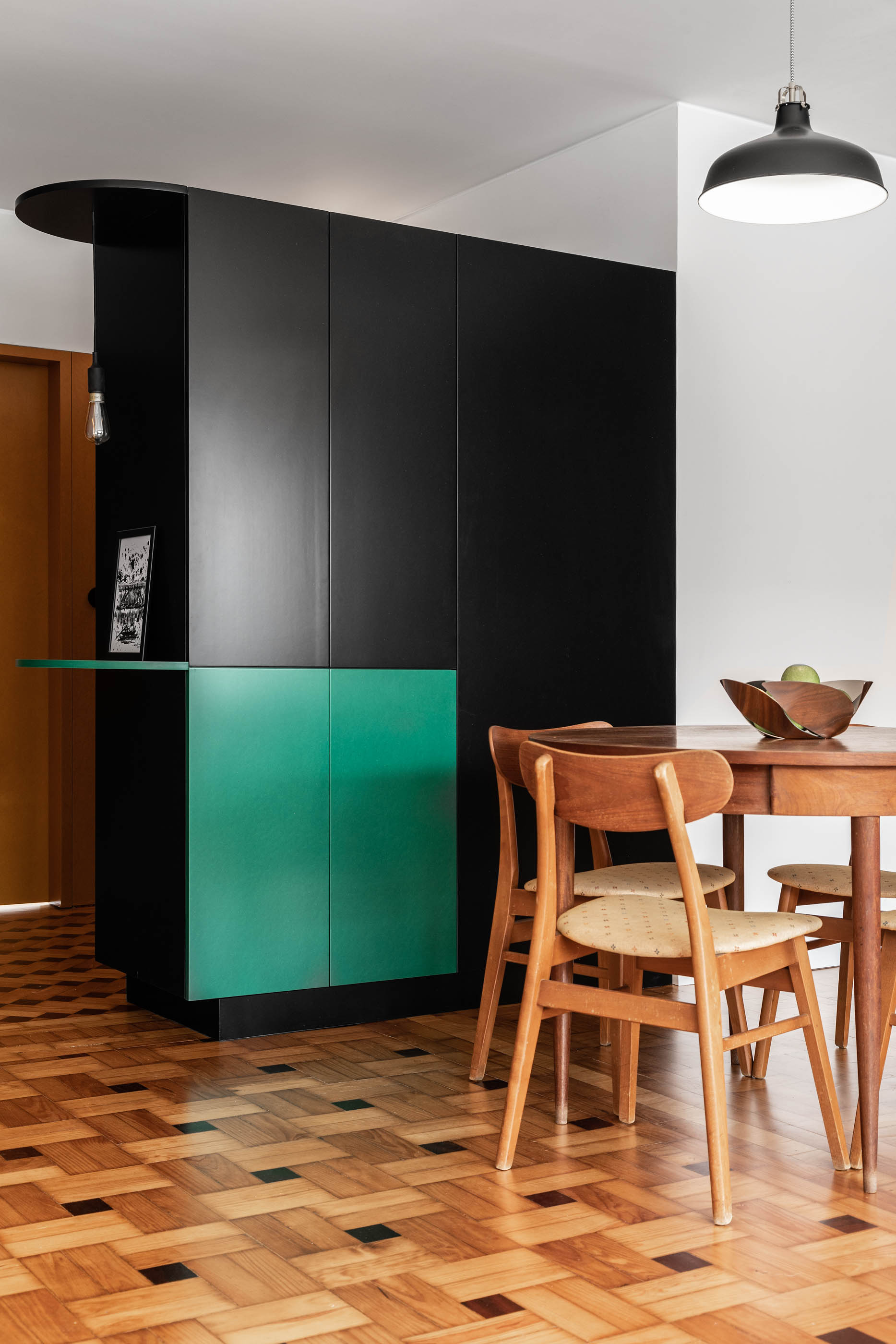 Detalhe de mesa de jantar com cadeiras de madeira e armário preto e verde ao fundo. — Apartamento Morro arquitetura Hinterland Architecture Studio em Vila Nova de Gaia