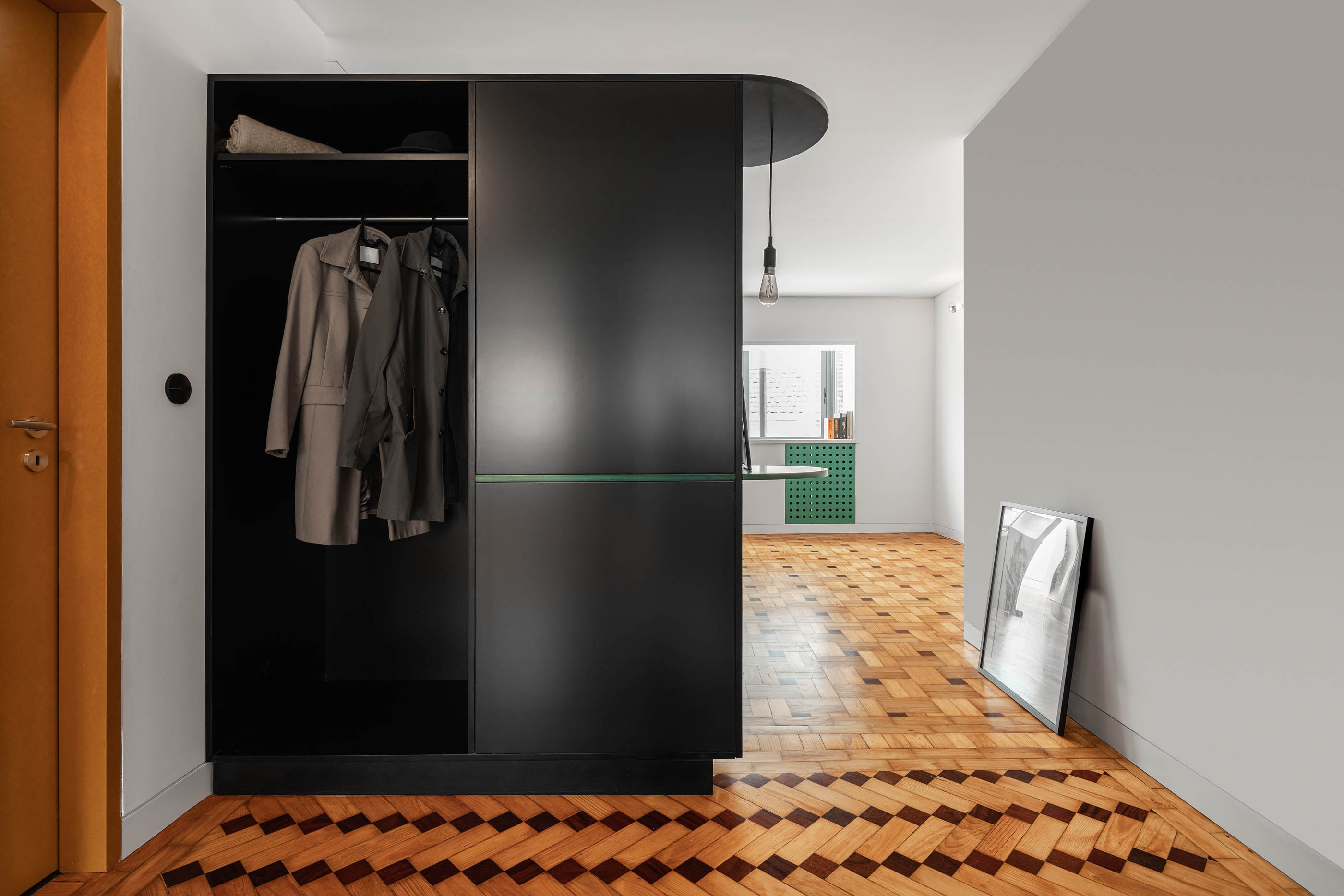 Armário preto com porta aberta, pavimento em madeira e vista para a sala de estar. — Apartamento Morro arquitetura Hinterland Architecture Studio em Vila Nova de Gaia