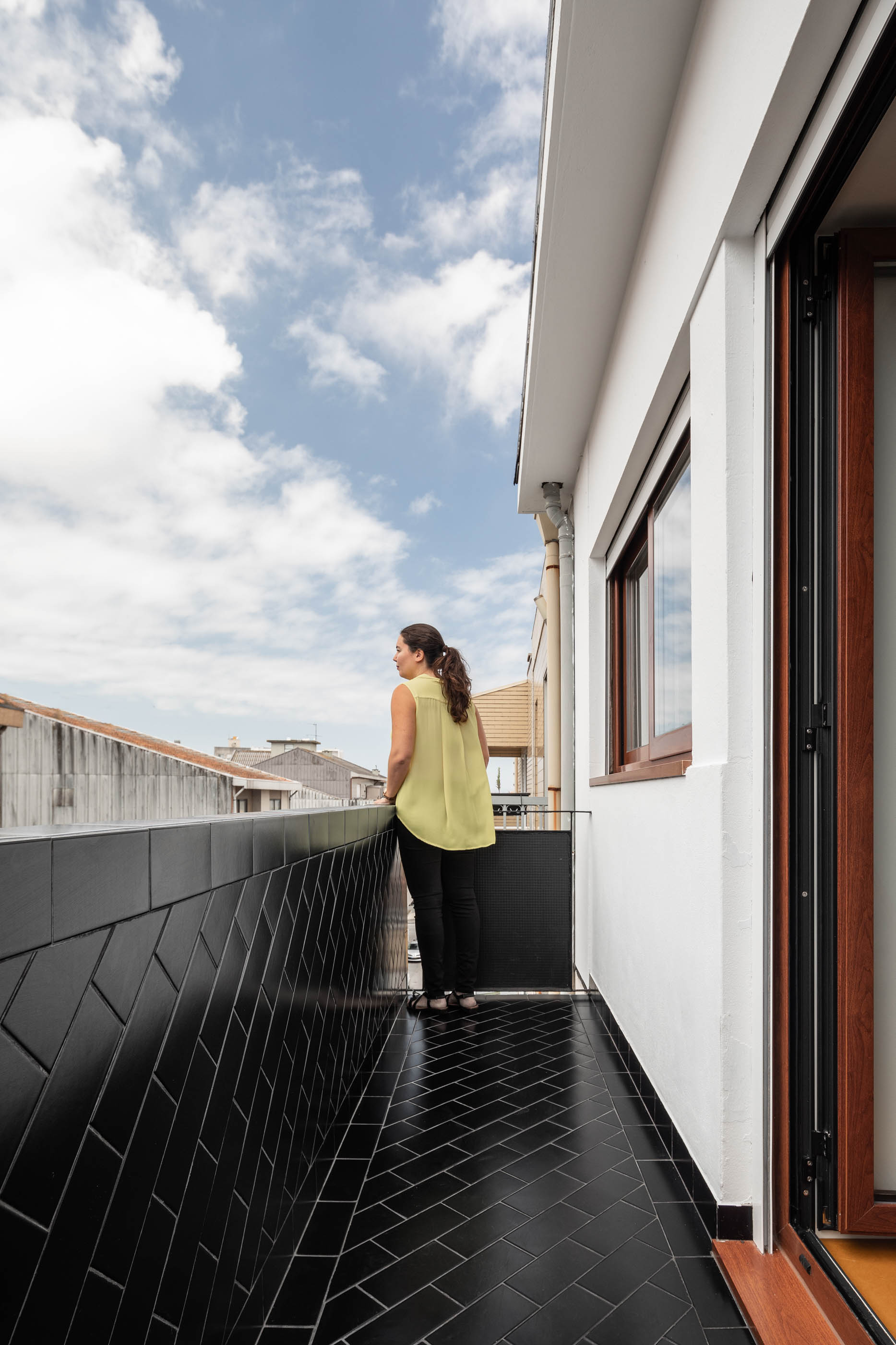 Varanda com pavimento em cerâmica preta, guarda corpo em tijoleira preta e vista para a cidade. — Apartamento Morro arquitetura Hinterland Architecture Studio em Vila Nova de Gaia