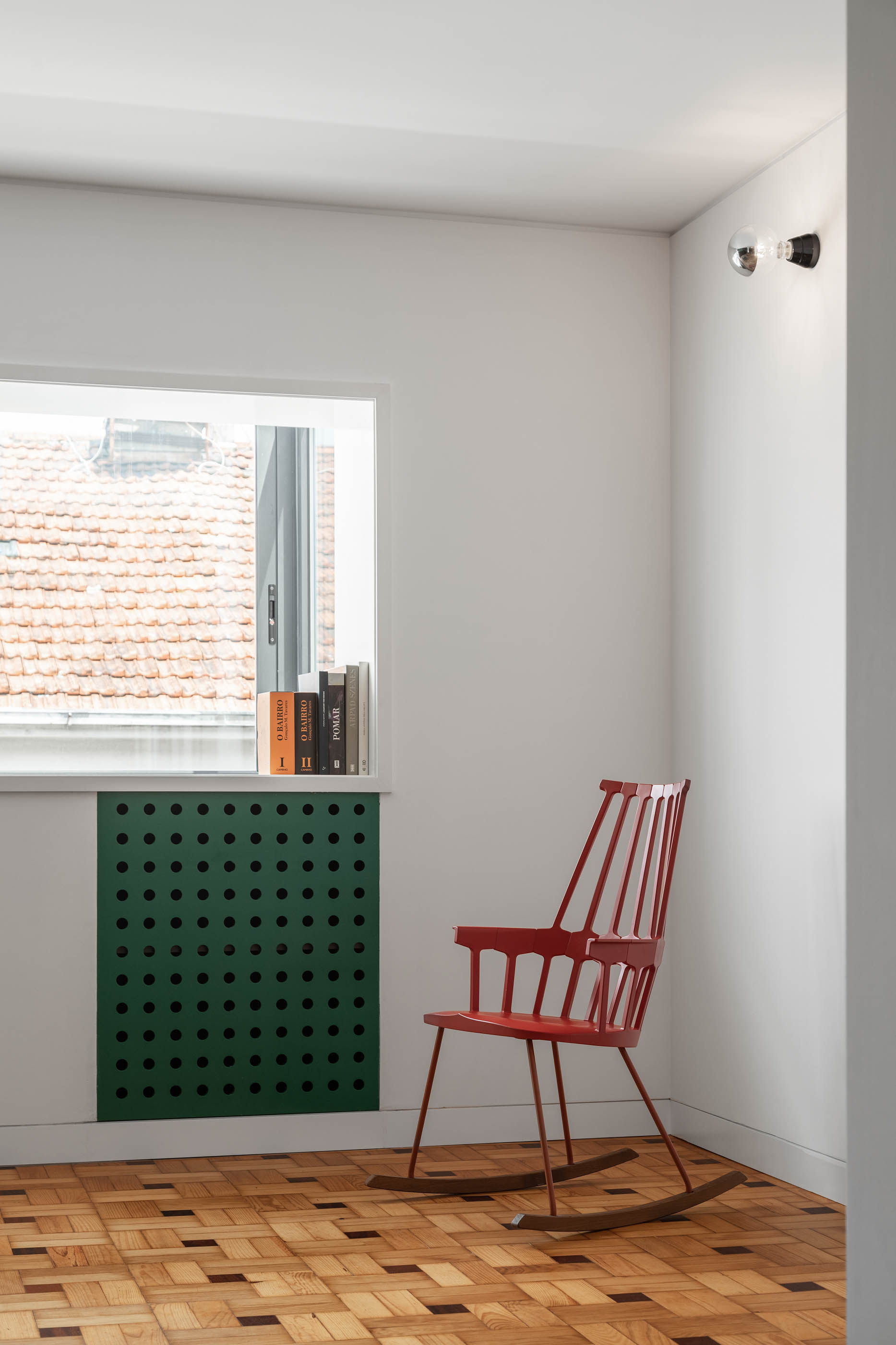 Quarto com cadeira de baloiço vermelha, radiador verde e pavimento em madeira com padrão geométrico. — Apartamento Morro arquitetura Hinterland Architecture Studio em Vila Nova de Gaia