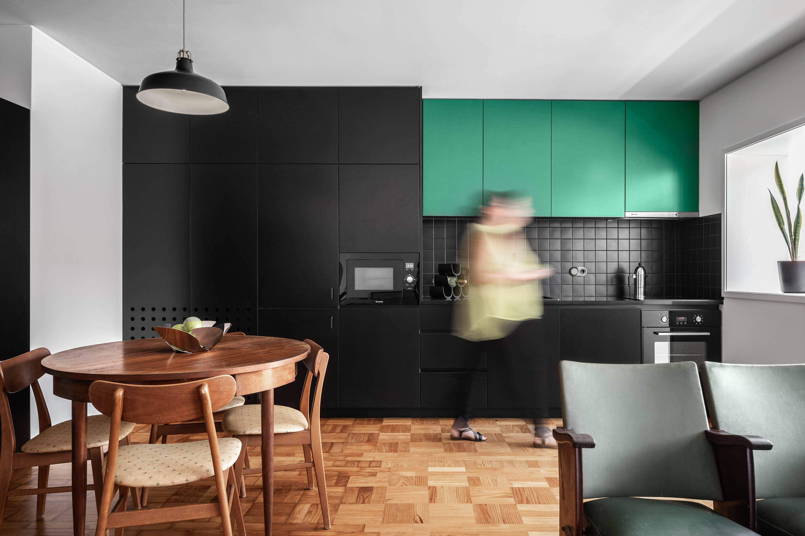 Cozinha com armários pretos e verdes, mesa de jantar redonda e pavimento em madeira. — Apartamento Morro arquitetura Hinterland Architecture Studio em Vila Nova de Gaia