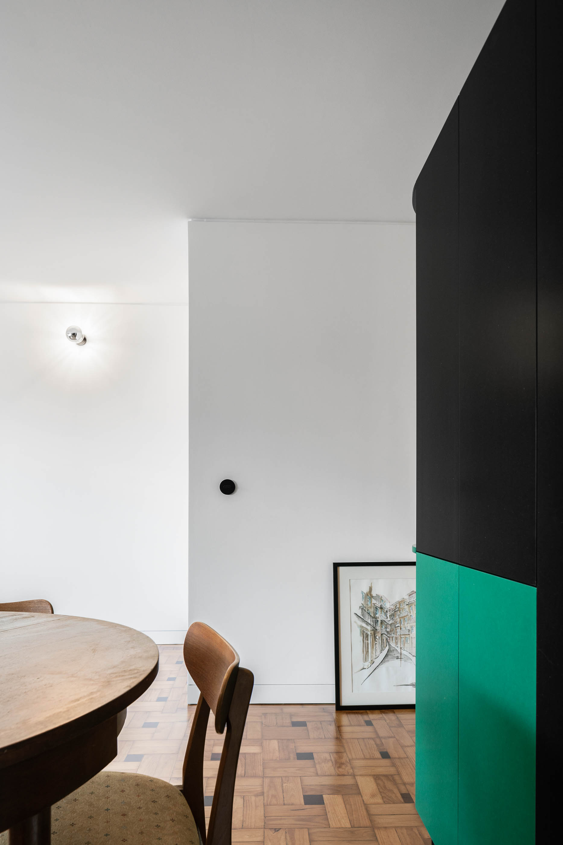 Detalhe de sala de jantar com mesa redonda, cadeira de madeira e armário preto e verde. — Apartamento Morro arquitetura Hinterland Architecture Studio em Vila Nova de Gaia