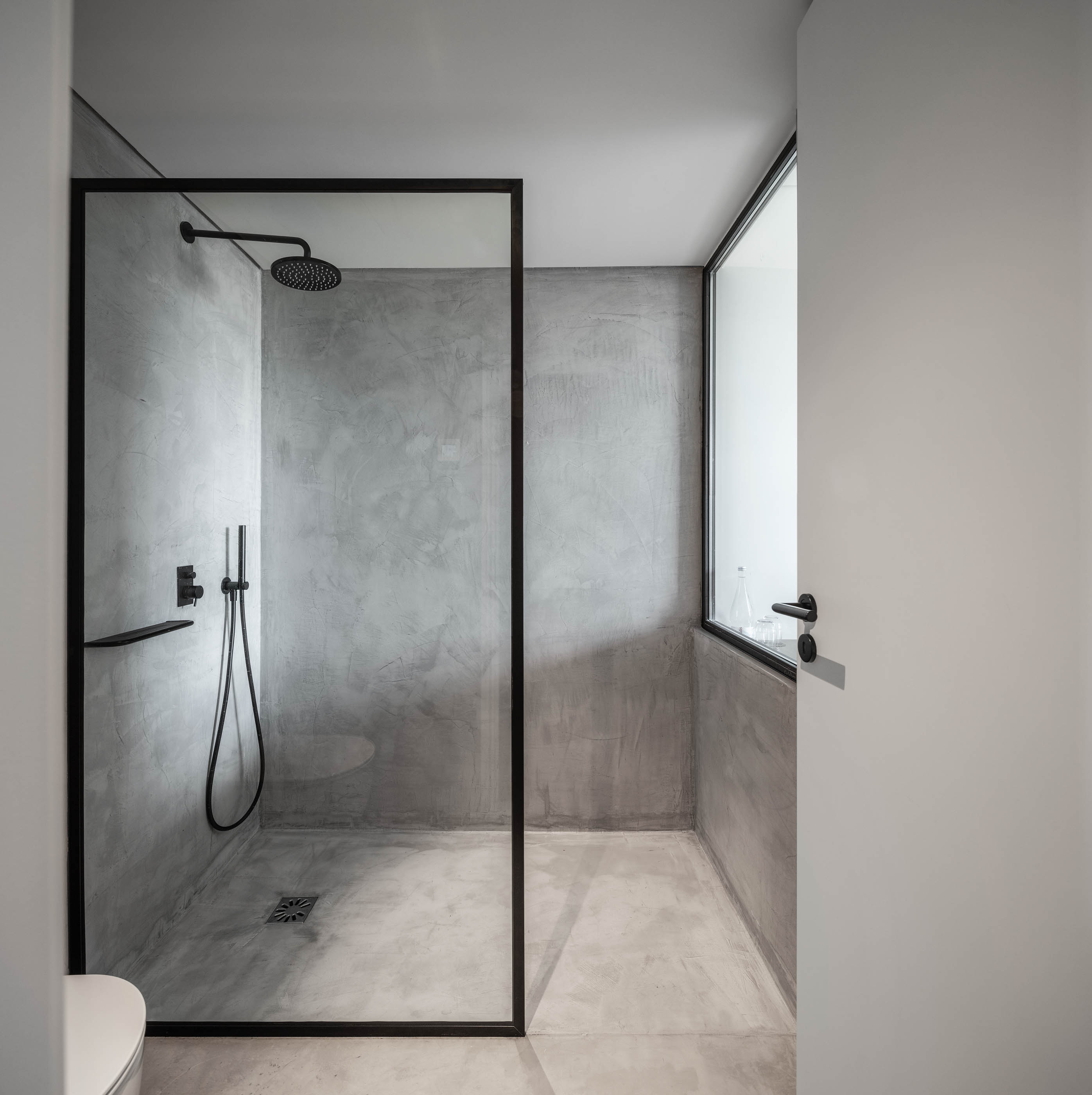 Casa de banho moderna com duche em betão aparente e divisória em vidro preto. — Exmo Hotel arquitetura Floret Arquitectura em Porto