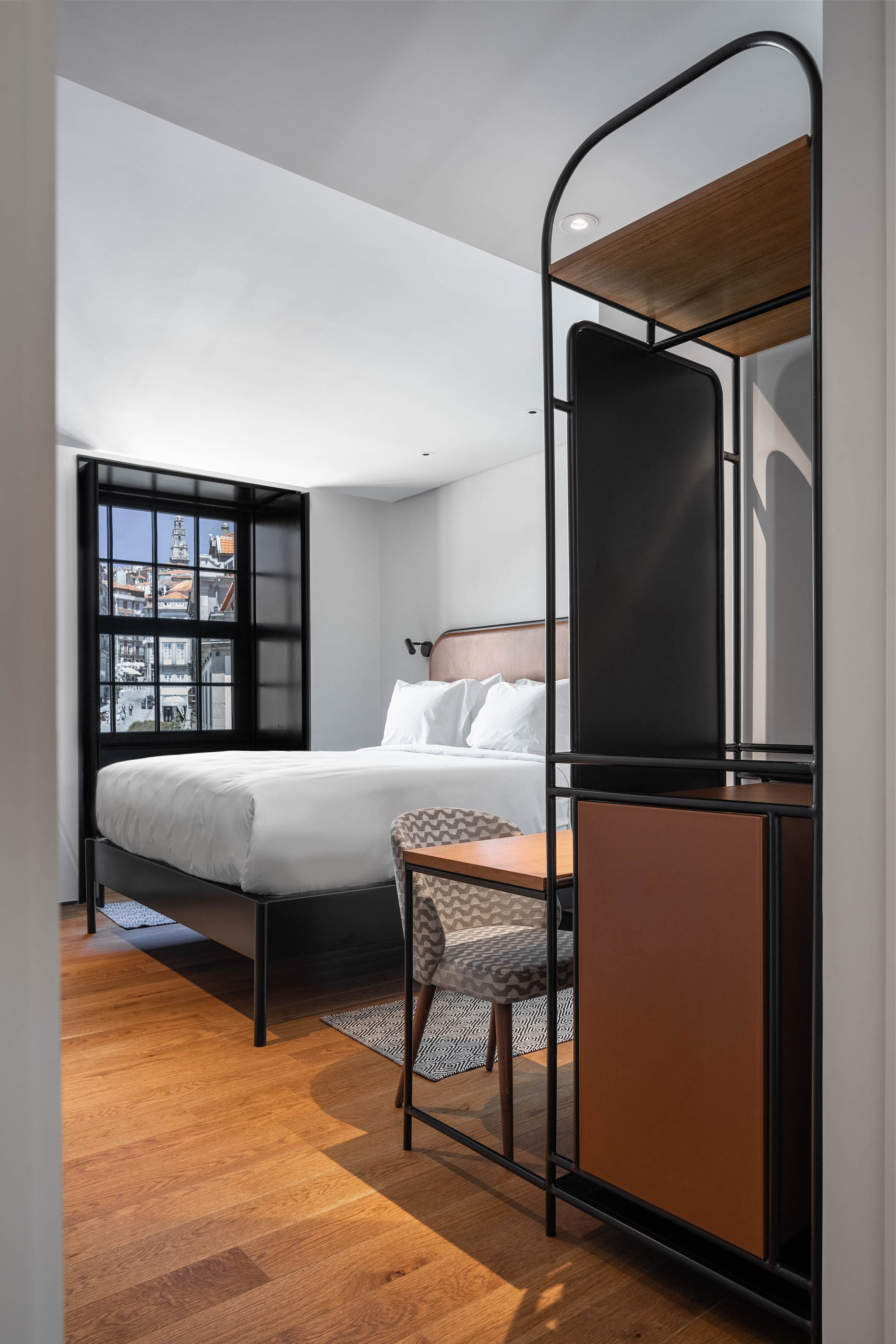 Quarto de hotel com cama de casal, secretária e estrutura metálica com prateleiras em madeira. — Exmo Hotel arquitetura Floret Arquitectura em Porto