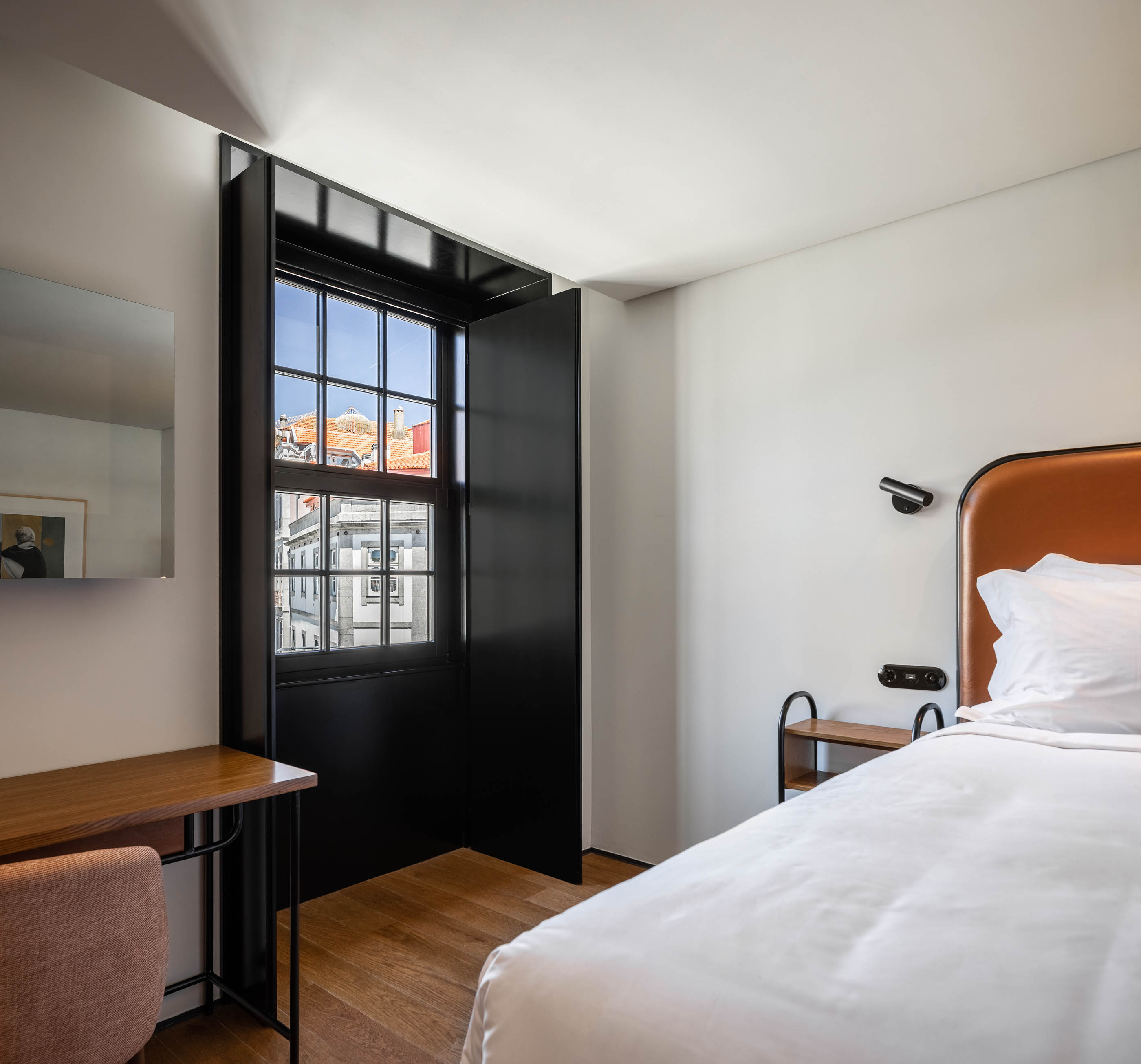 Quarto de hotel luminoso com cama de casal, secretária em madeira e janela com vista para a cidade. — Exmo Hotel arquitetura Floret Arquitectura em Porto
