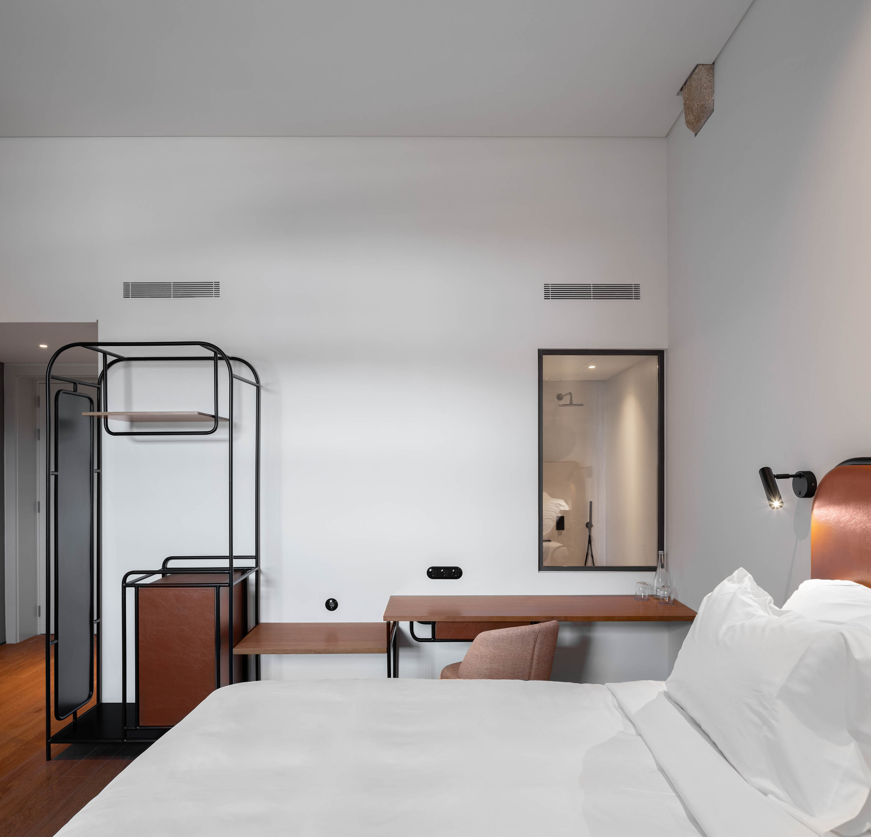 Quarto de hotel com cama de casal, secretária em madeira e espelho, design minimalista e funcional. — Exmo Hotel arquitetura Floret Arquitectura em Porto