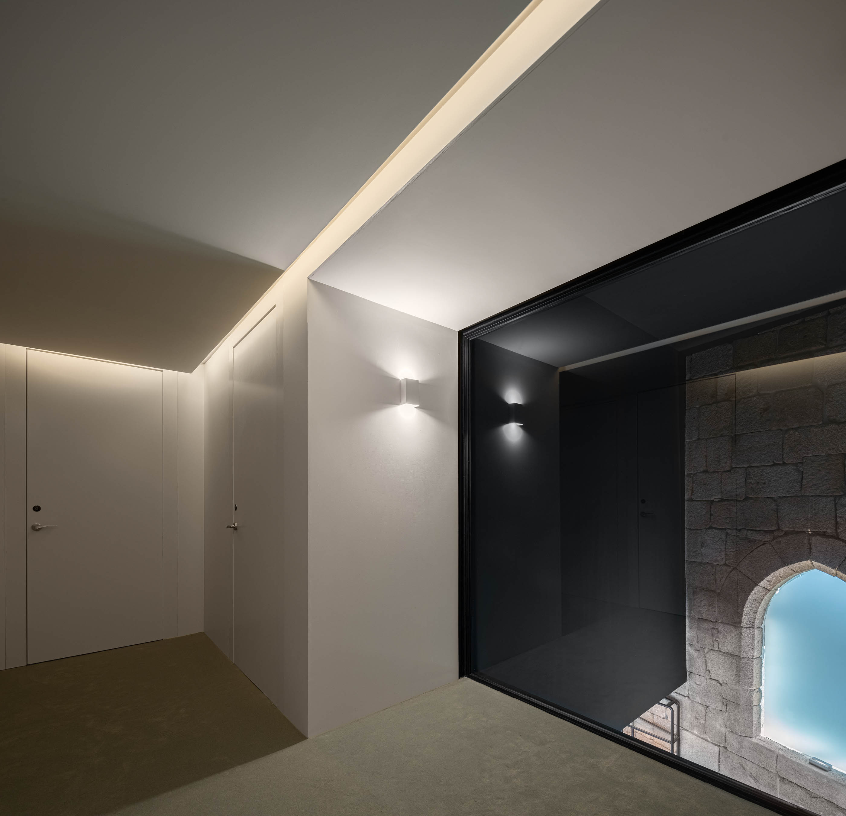 Corredor branco com iluminação embutida e vista para o espaço do bar através de uma abertura envidraçada. — Exmo Hotel arquitetura Floret Arquitectura em Porto