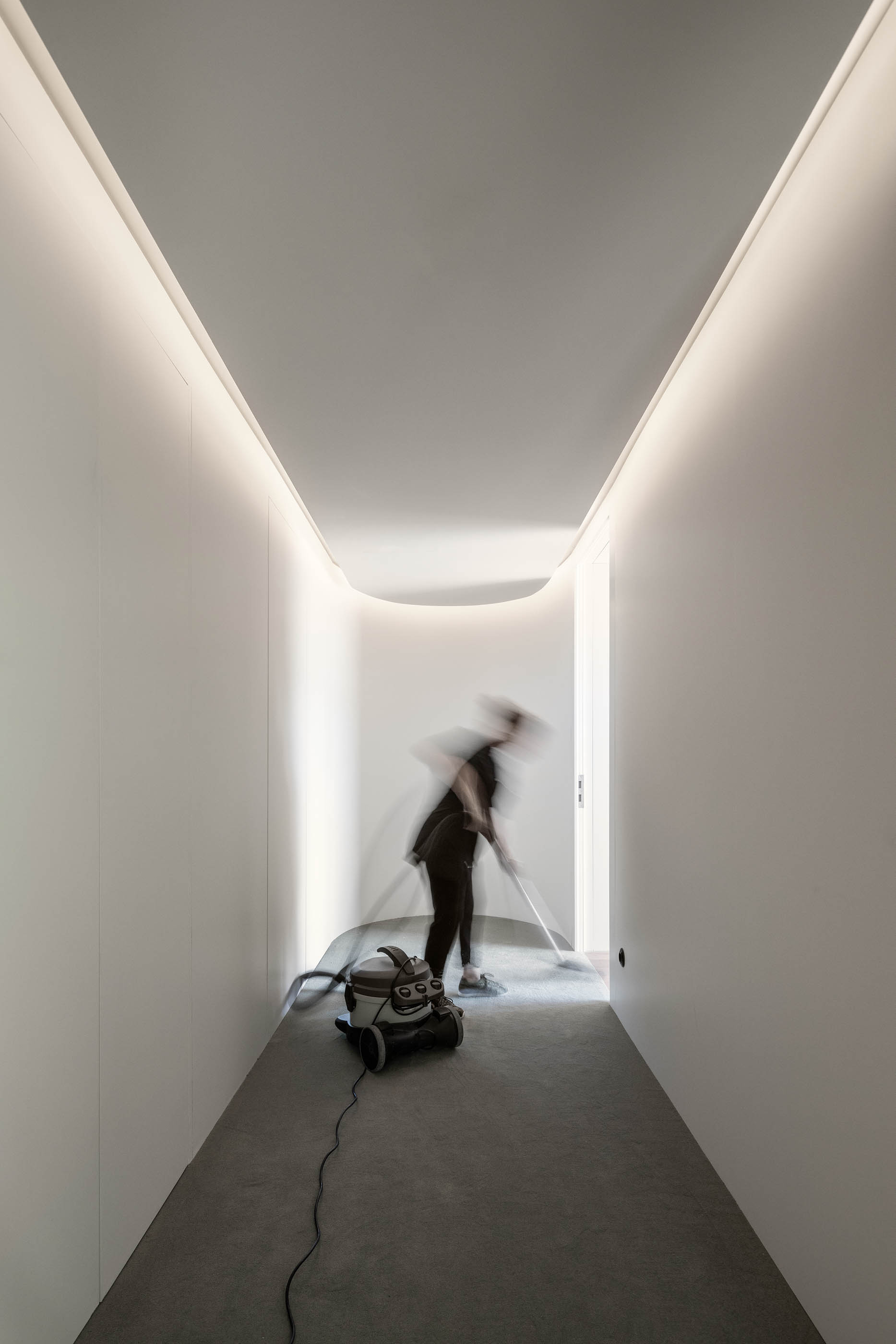 Corredor minimalista branco com iluminação linear e funcionária a limpar o chão. — Exmo Hotel arquitetura Floret Arquitectura em Porto