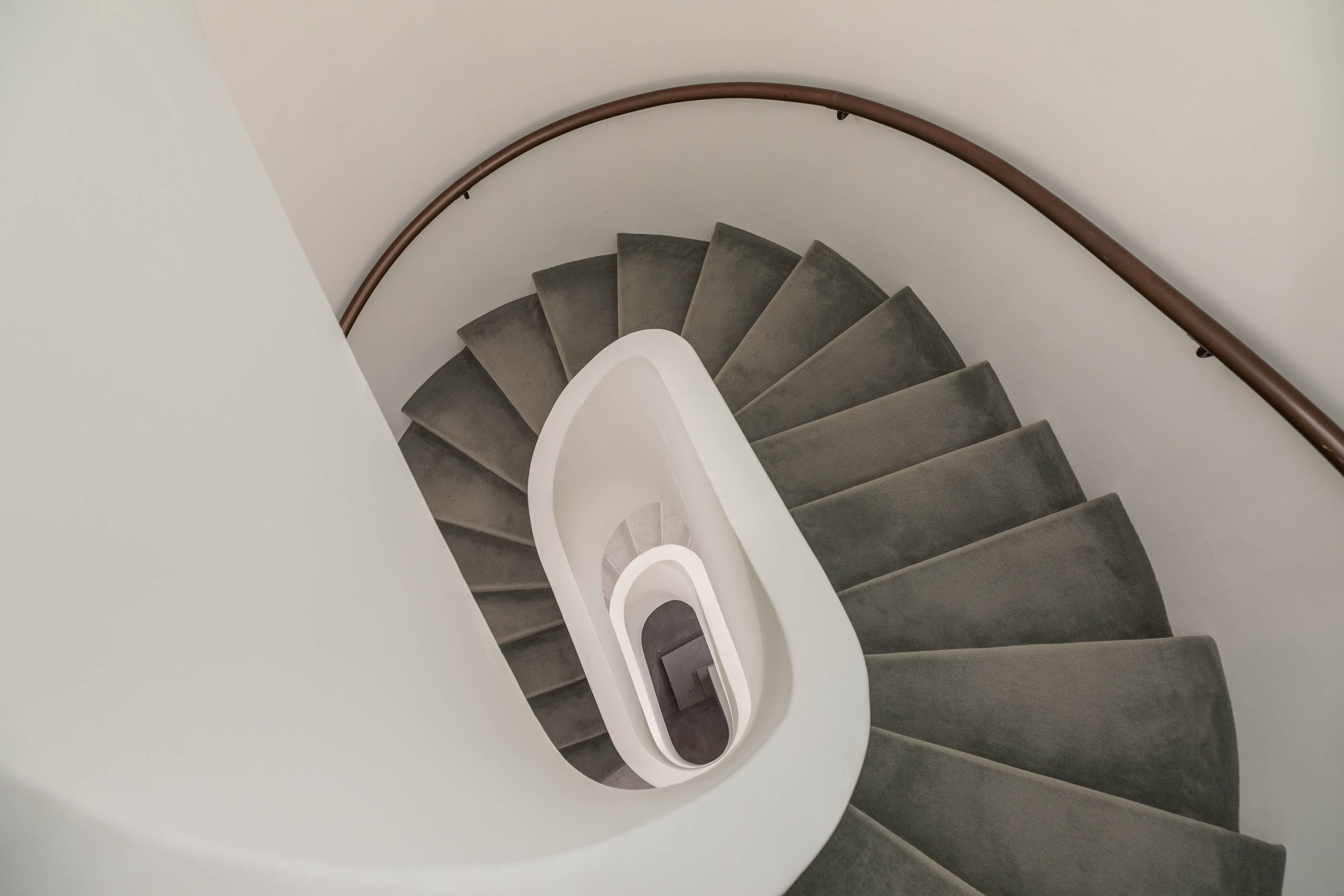 Vista superior da escadaria em caracol com corrimão em madeira e degraus revestidos a carpete cinzenta. — Exmo Hotel arquitetura Floret Arquitectura em Porto
