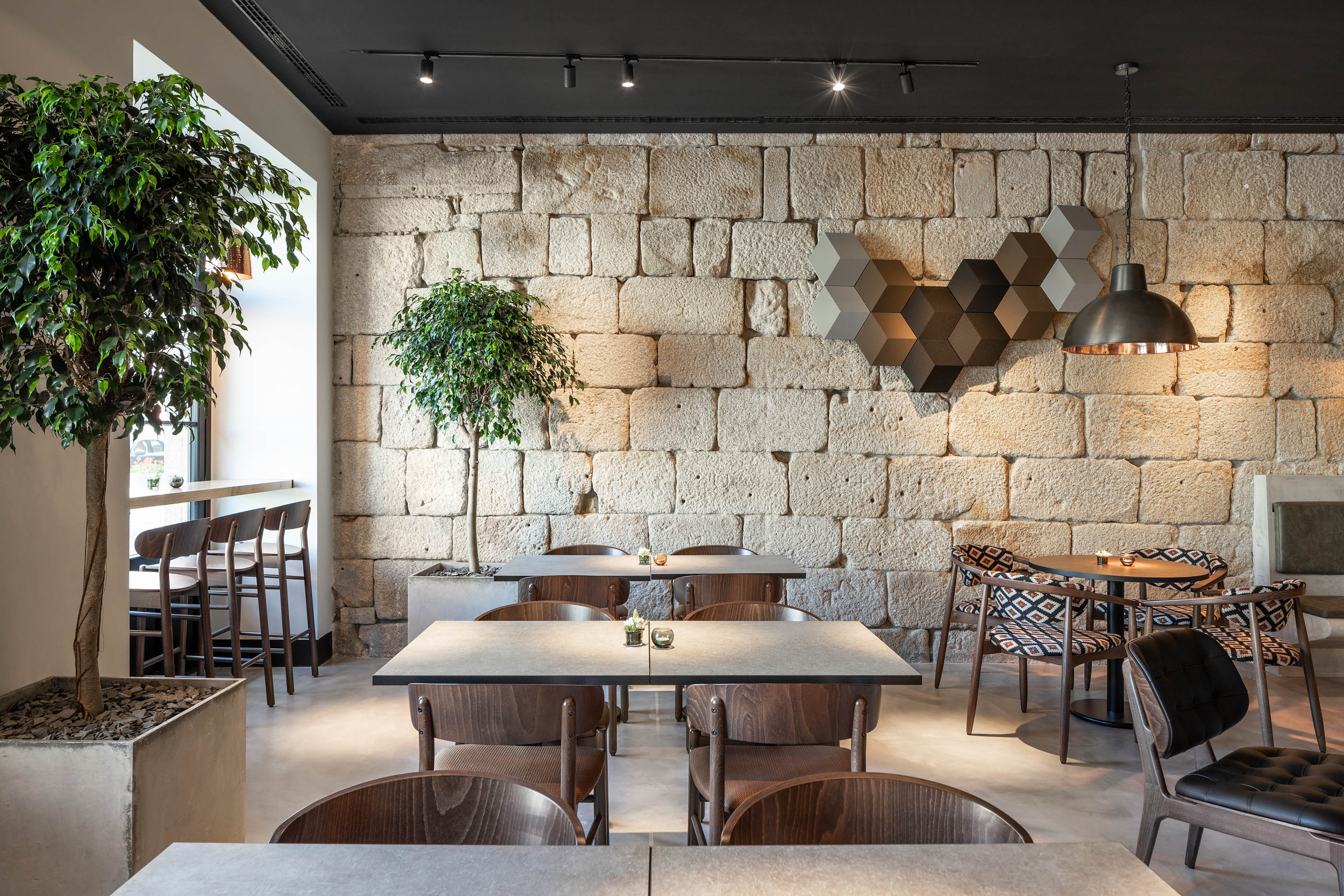 Restaurante com paredes em pedra original, mesas em madeira e cadeiras de design, ambiente acolhedor. — Exmo Hotel arquitetura Floret Arquitectura em Porto