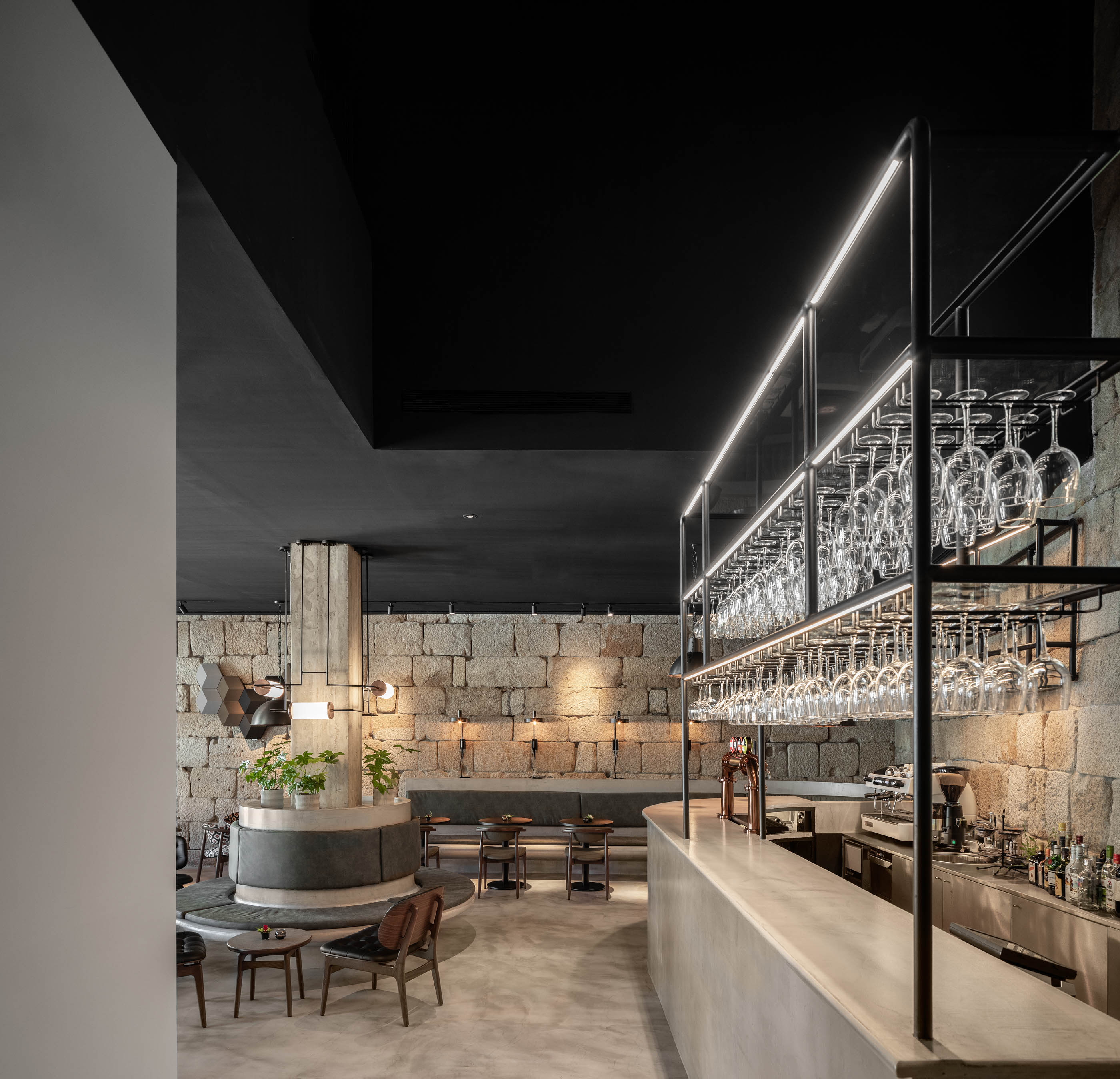 Bar com balcão em mármore, prateleiras metálicas com copos e paredes em pedra original, iluminação suave. — Exmo Hotel arquitetura Floret Arquitectura em Porto