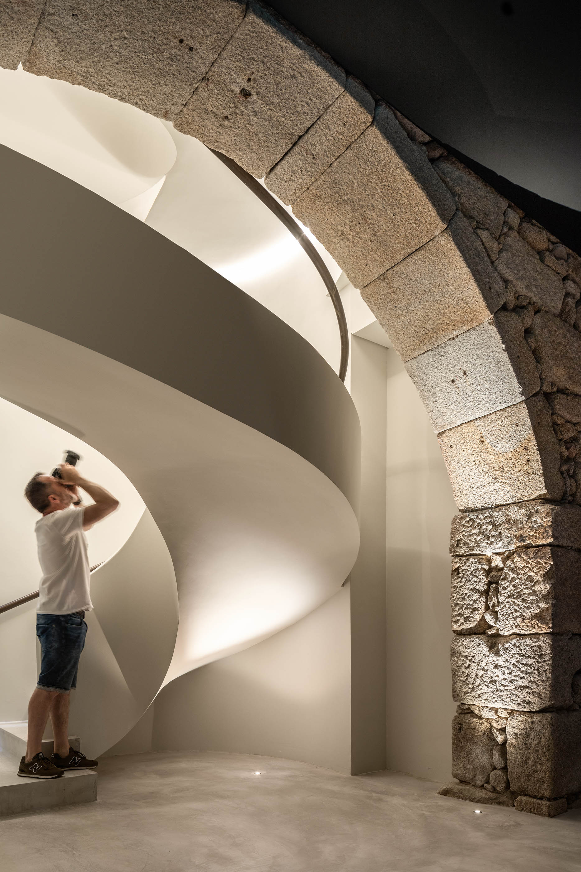 Homem a fotografar a escadaria em espiral através de um arco em pedra original, preservação da história. — Exmo Hotel arquitetura Floret Arquitectura em Porto