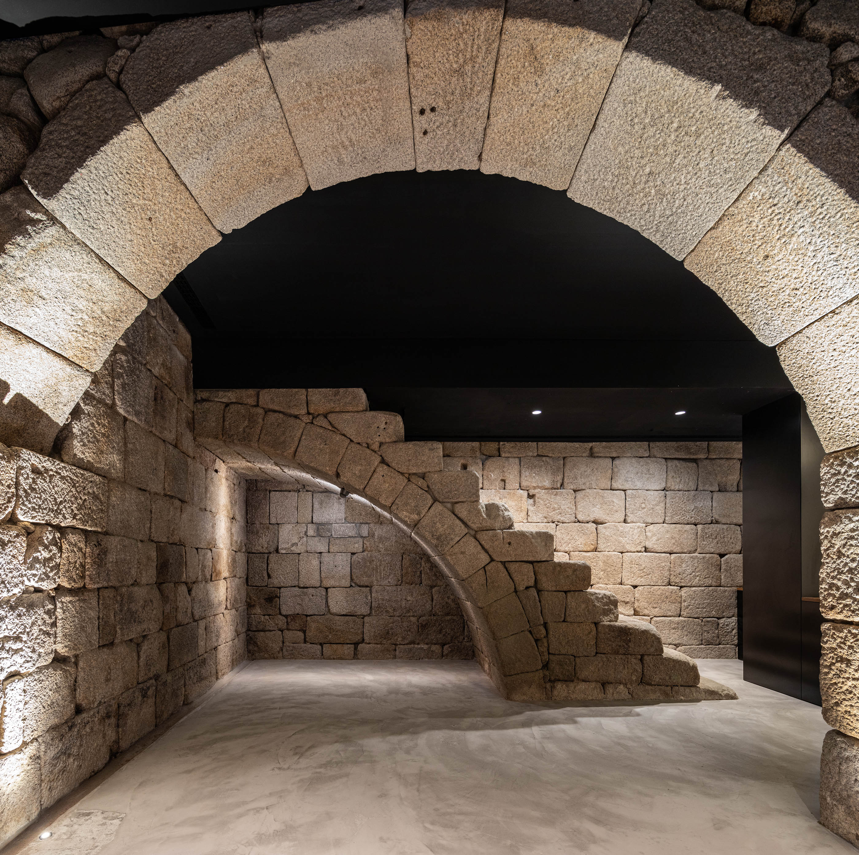 Espaço com paredes em pedra original, escadaria em pedra e iluminação moderna, ambiente histórico. — Exmo Hotel arquitetura Floret Arquitectura em Porto