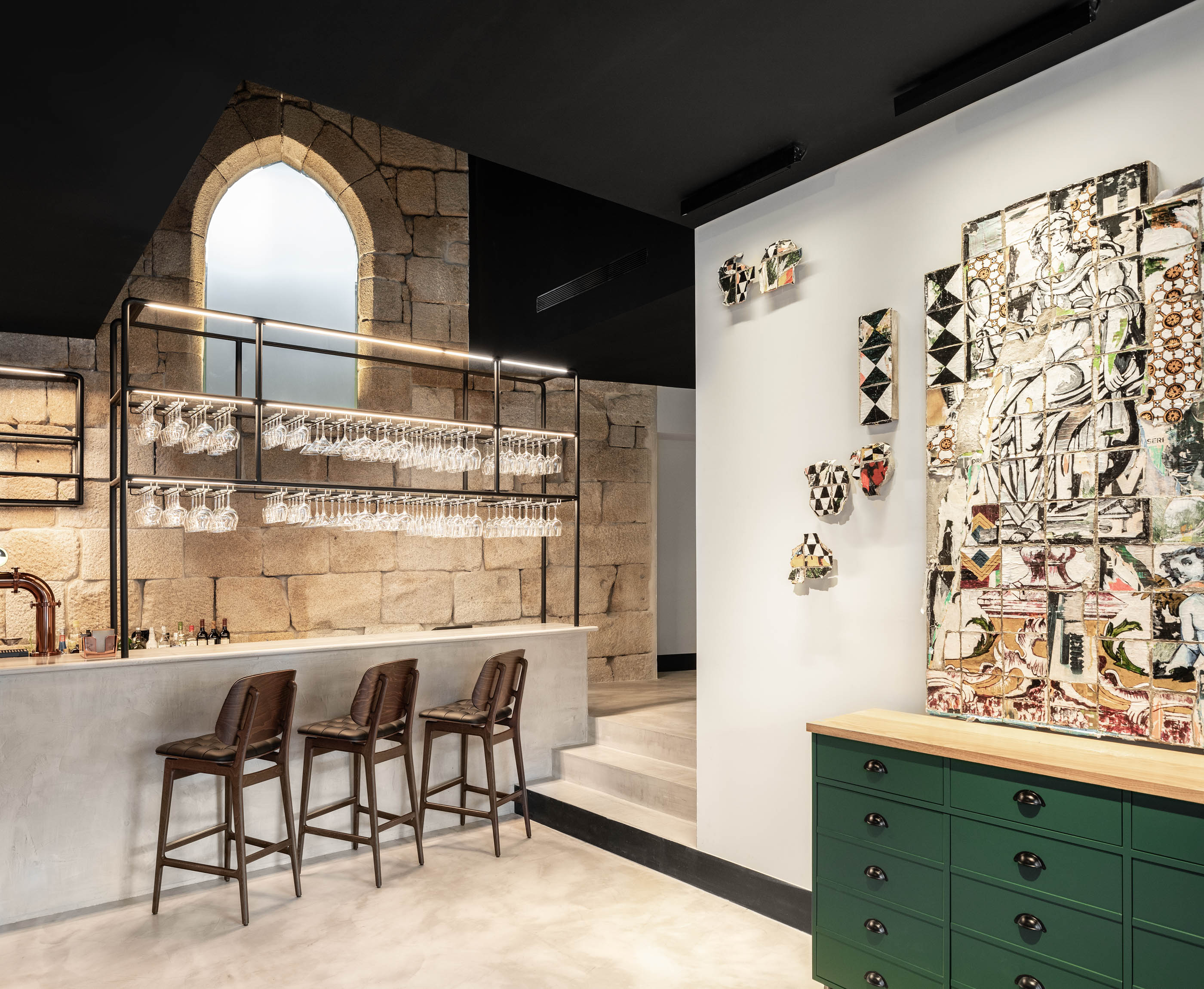 Bar com paredes em pedra original, prateleiras metálicas com copos e obras de arte modernas, ambiente eclético. — Exmo Hotel arquitetura Floret Arquitectura em Porto