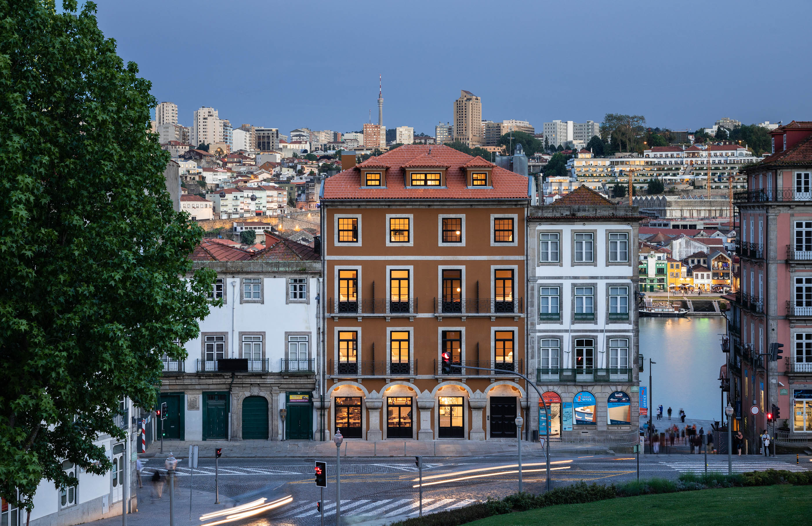 Vista noturna da fachada do hotel e da cidade do Porto, iluminação ambiente e movimento urbano. — Exmo Hotel arquitetura Floret Arquitectura em Porto