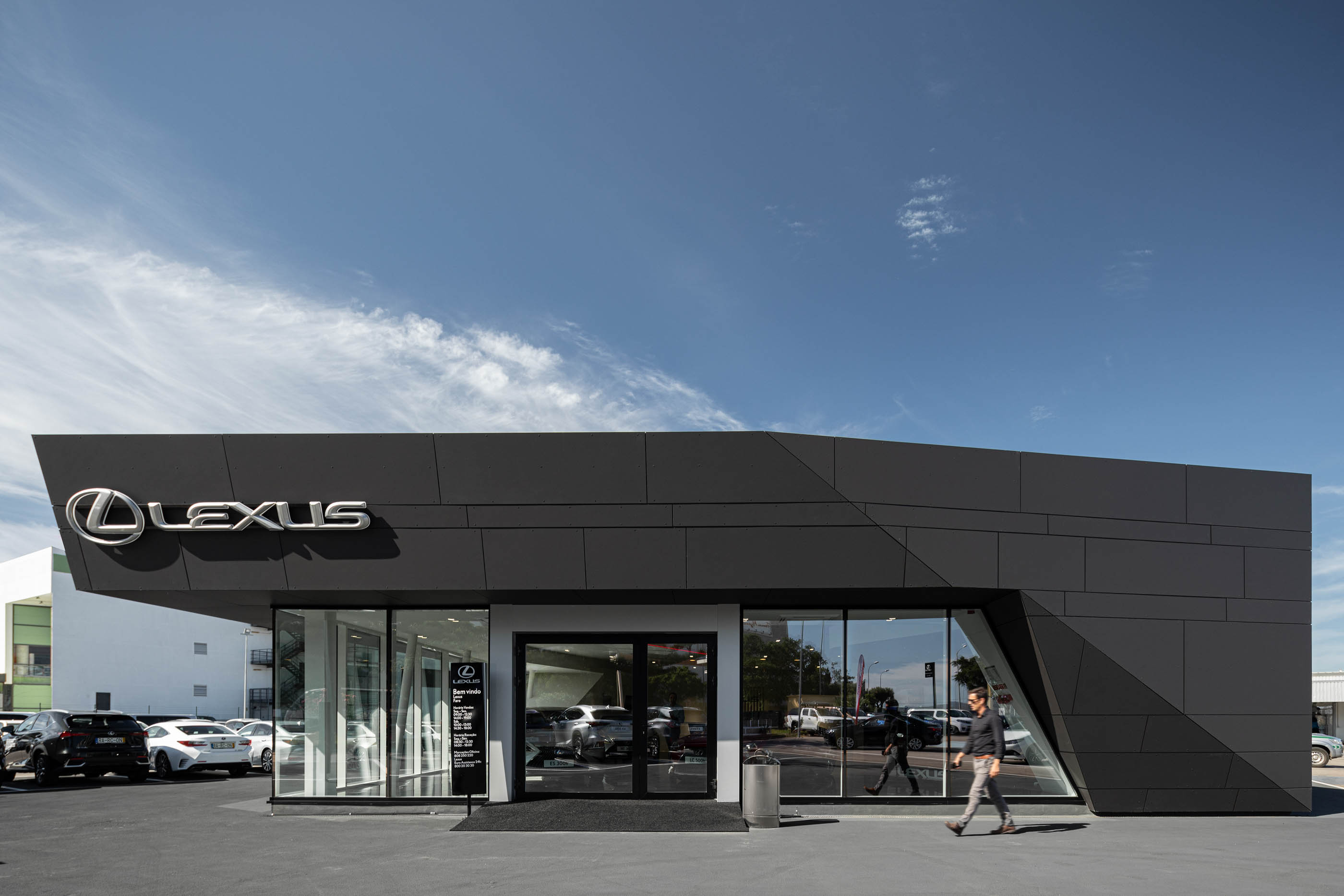 Divisão exterior do stand Lexus Faro, com revestimento em painéis escuros e grandes janelas, estilo moderno e minimalista. — Stand Lexus Faro arquitetura Rarcon Arquitectura em Portugal