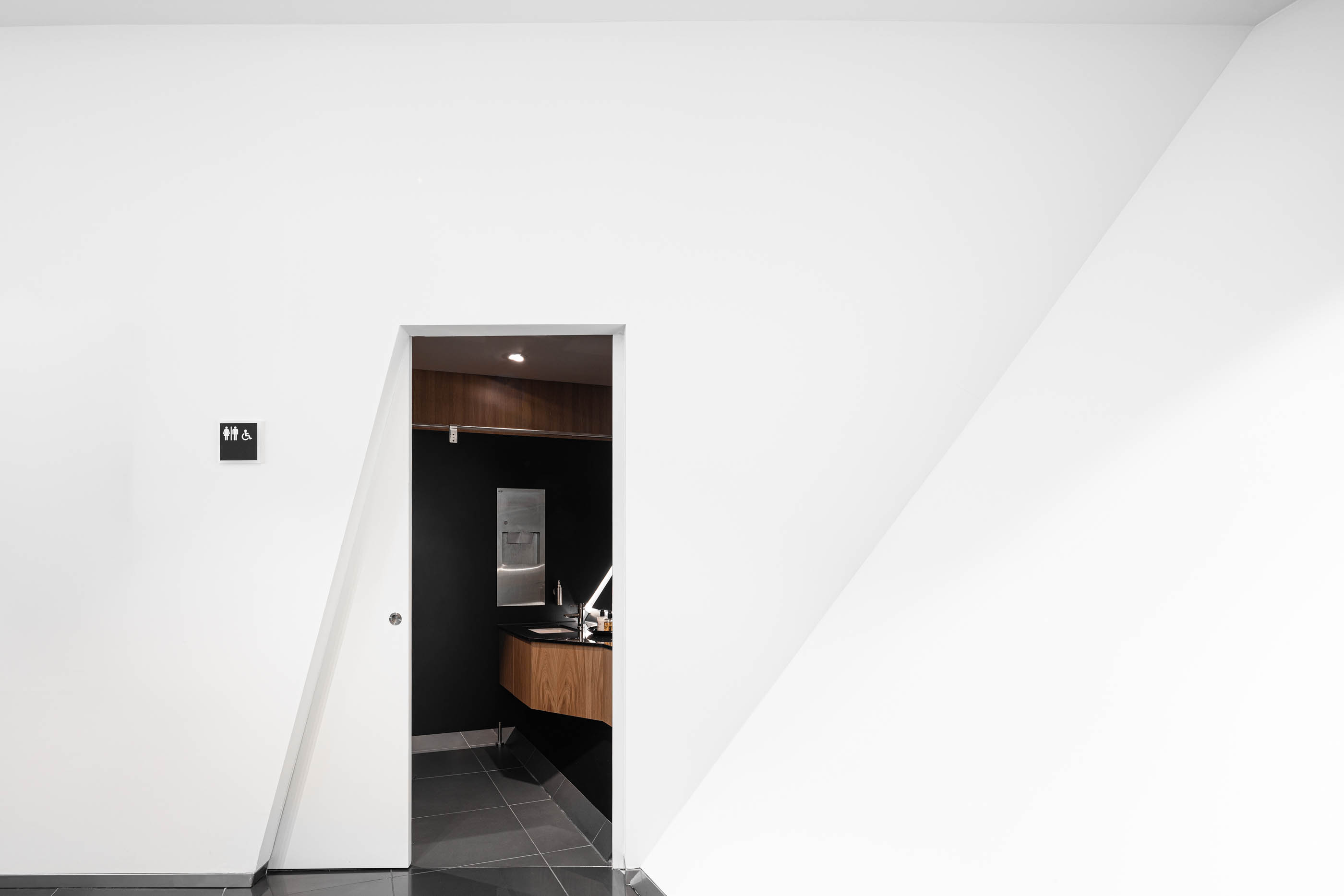Interior minimalista do stand Lexus, com porta para casa de banho, paredes brancas e detalhes em madeira. — Stand Lexus Faro arquitetura Rarcon Arquitectura em Portugal