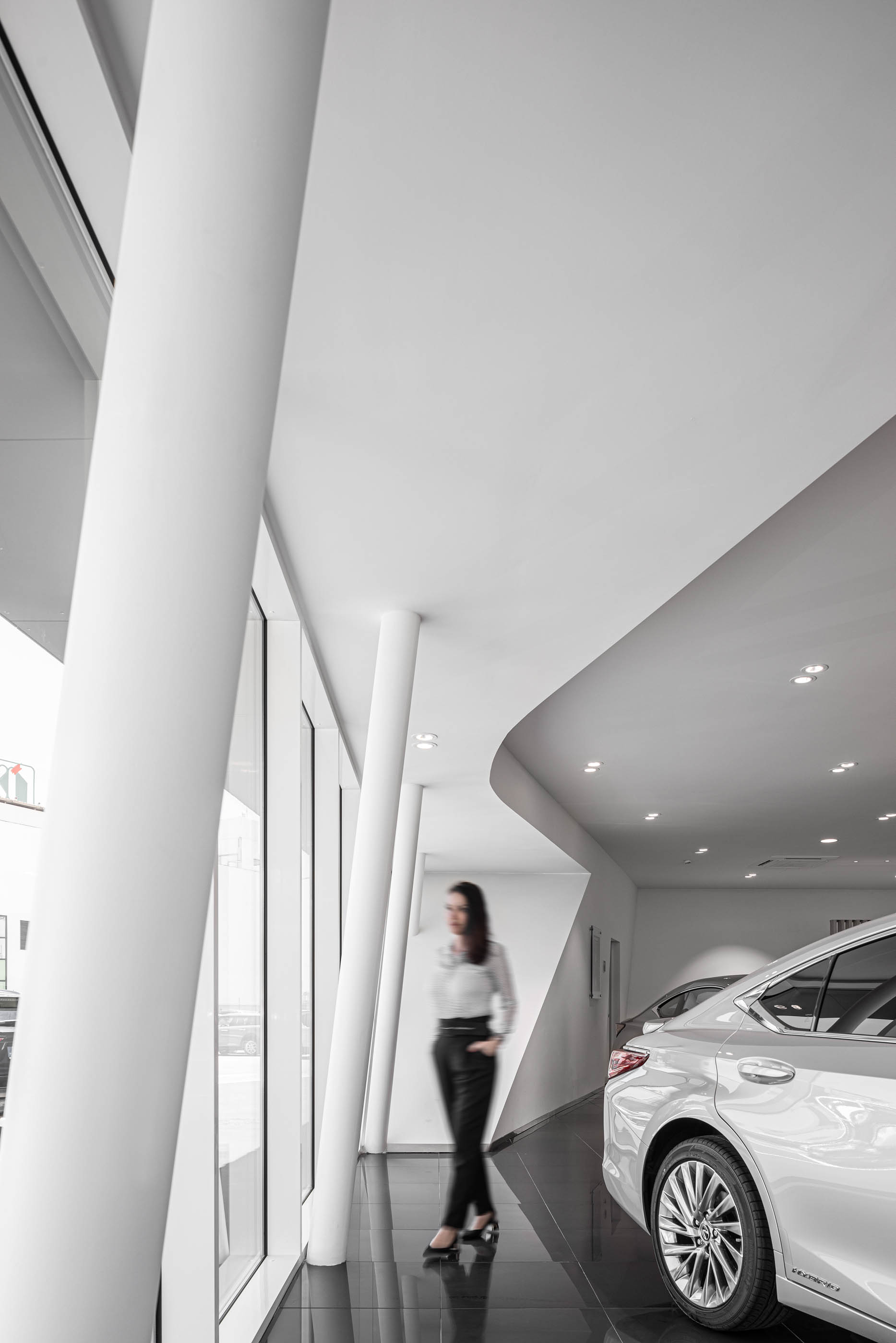 Interior do stand Lexus, com pilares brancos inclinados, grandes janelas e piso preto brilhante. — Stand Lexus Faro arquitetura Rarcon Arquitectura em Portugal