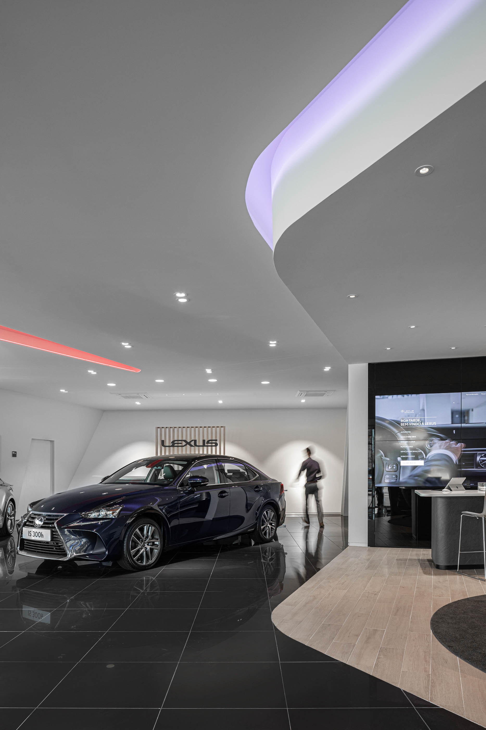 Interior do stand Lexus, com carros expostos, iluminação moderna e piso com diferentes materiais. — Stand Lexus Faro arquitetura Rarcon Arquitectura em Portugal