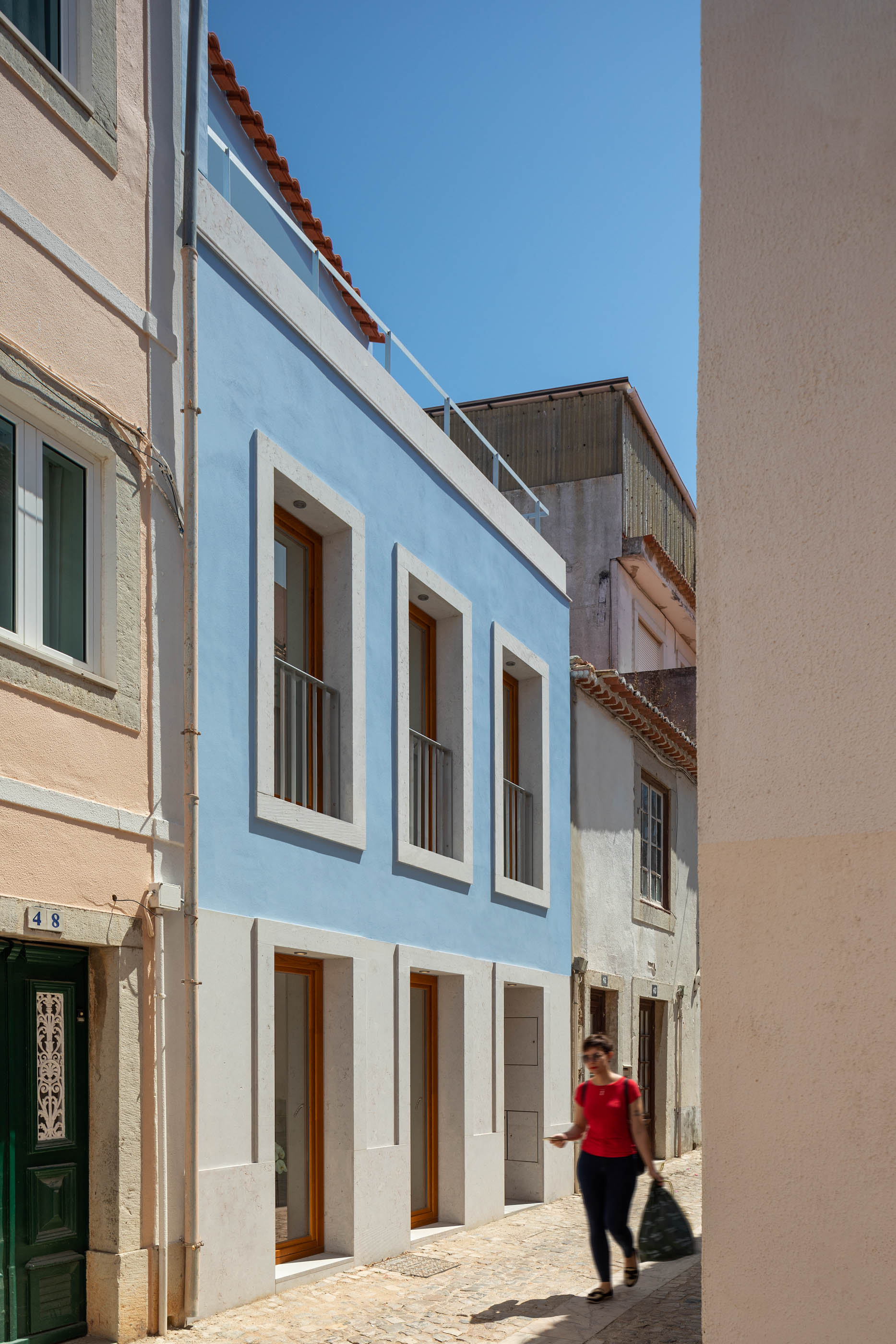 Fachada azul celeste de casa estreita, com molduras de pedra clara nas janelas e varanda no topo. — Casa GD arquitetura Esquissos Arquitectura em Portugal