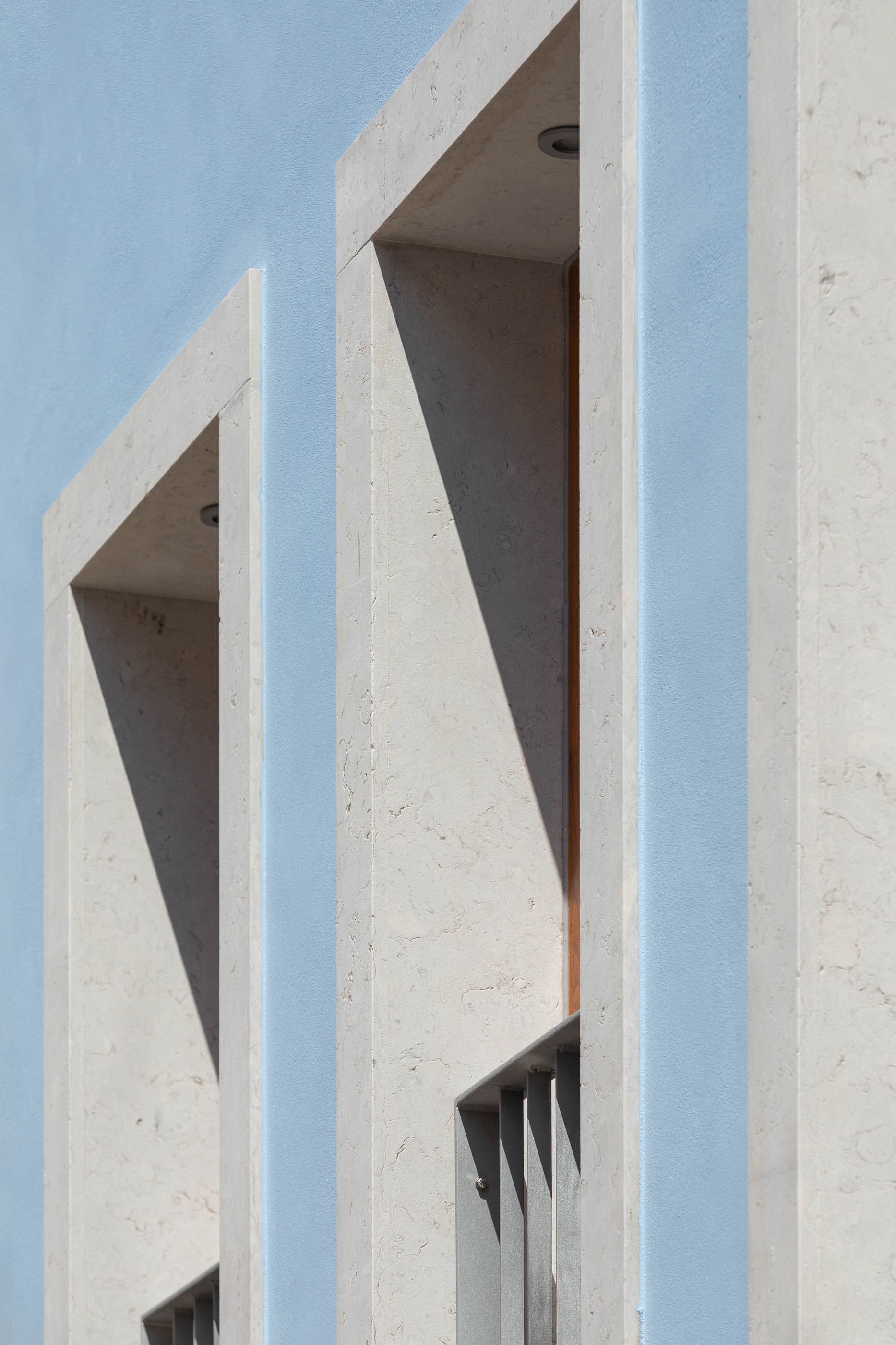 Detalhe de janelas embutidas em pedra clara, com sombras marcadas e fachada azul. — Casa GD arquitetura Esquissos Arquitectura em Portugal