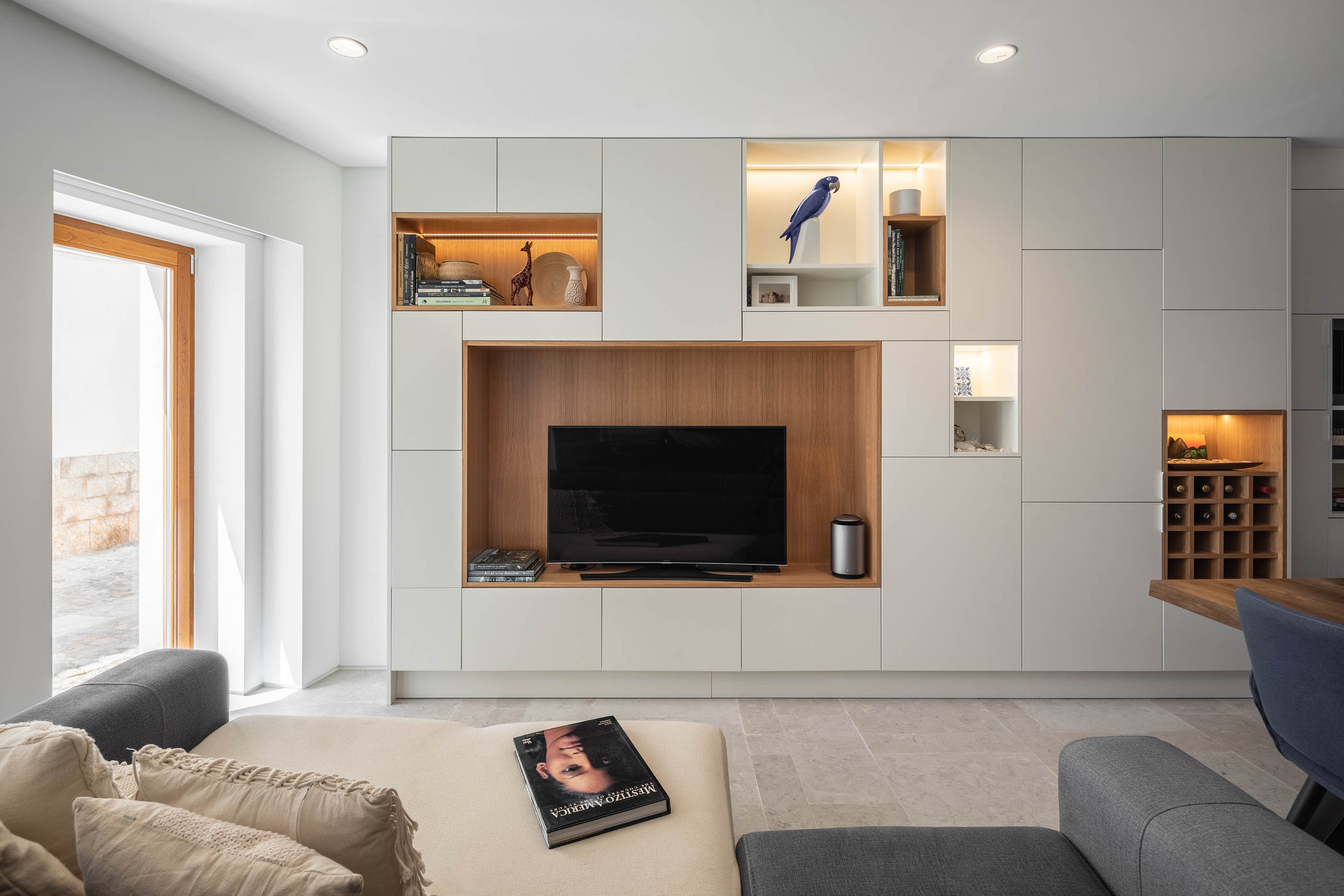 Sala de estar moderna com móveis embutidos brancos e madeira, sofá cinza e chão em pedra. — Casa GD arquitetura Esquissos Arquitectura em Portugal
