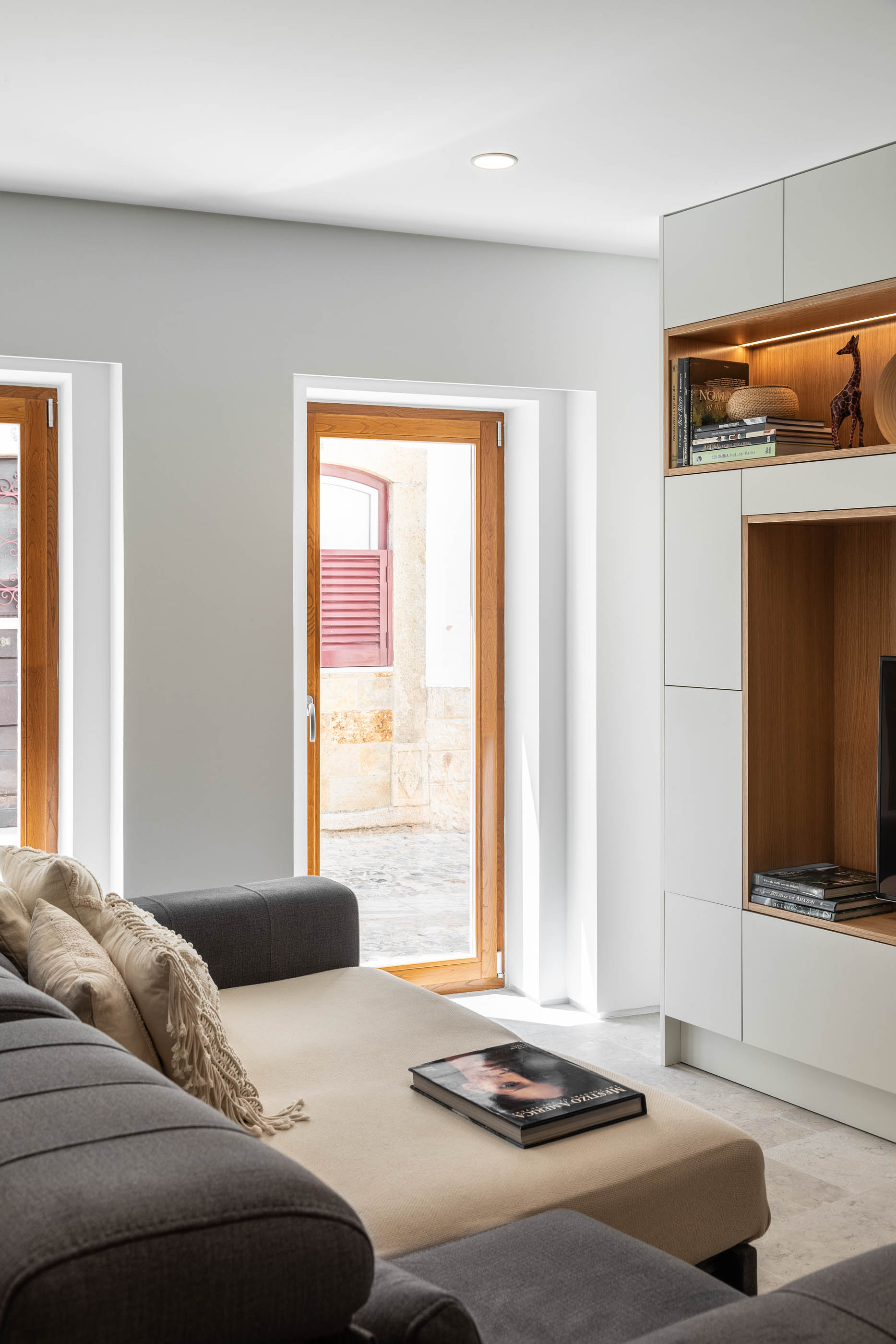 Sala de estar com sofá cinza, estante embutida e porta de madeira que dá para a rua. — Casa GD arquitetura Esquissos Arquitectura em Portugal