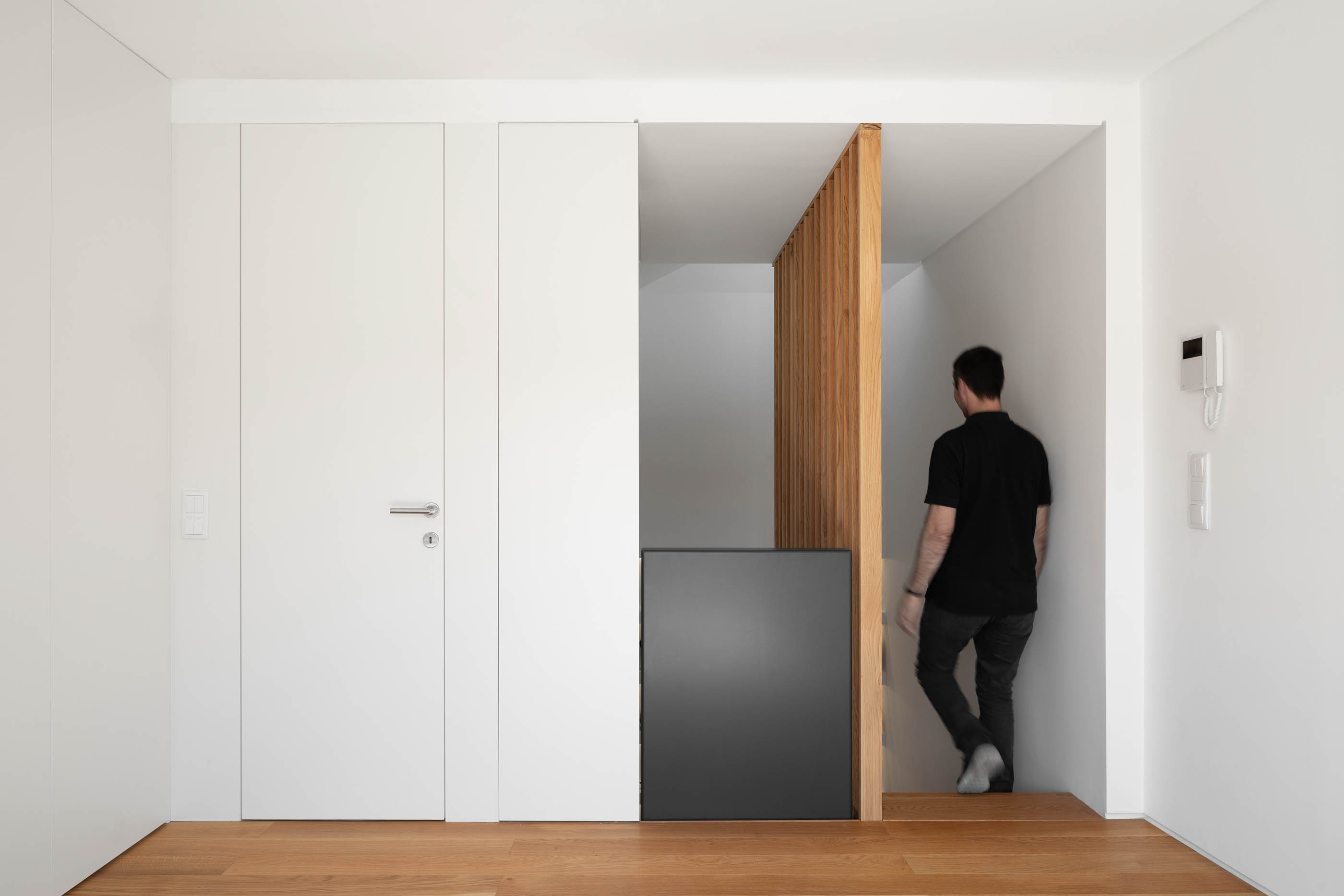 Hall de entrada com porta branca, escada de madeira e armário preto. — Casa GD arquitetura Esquissos Arquitectura em Portugal