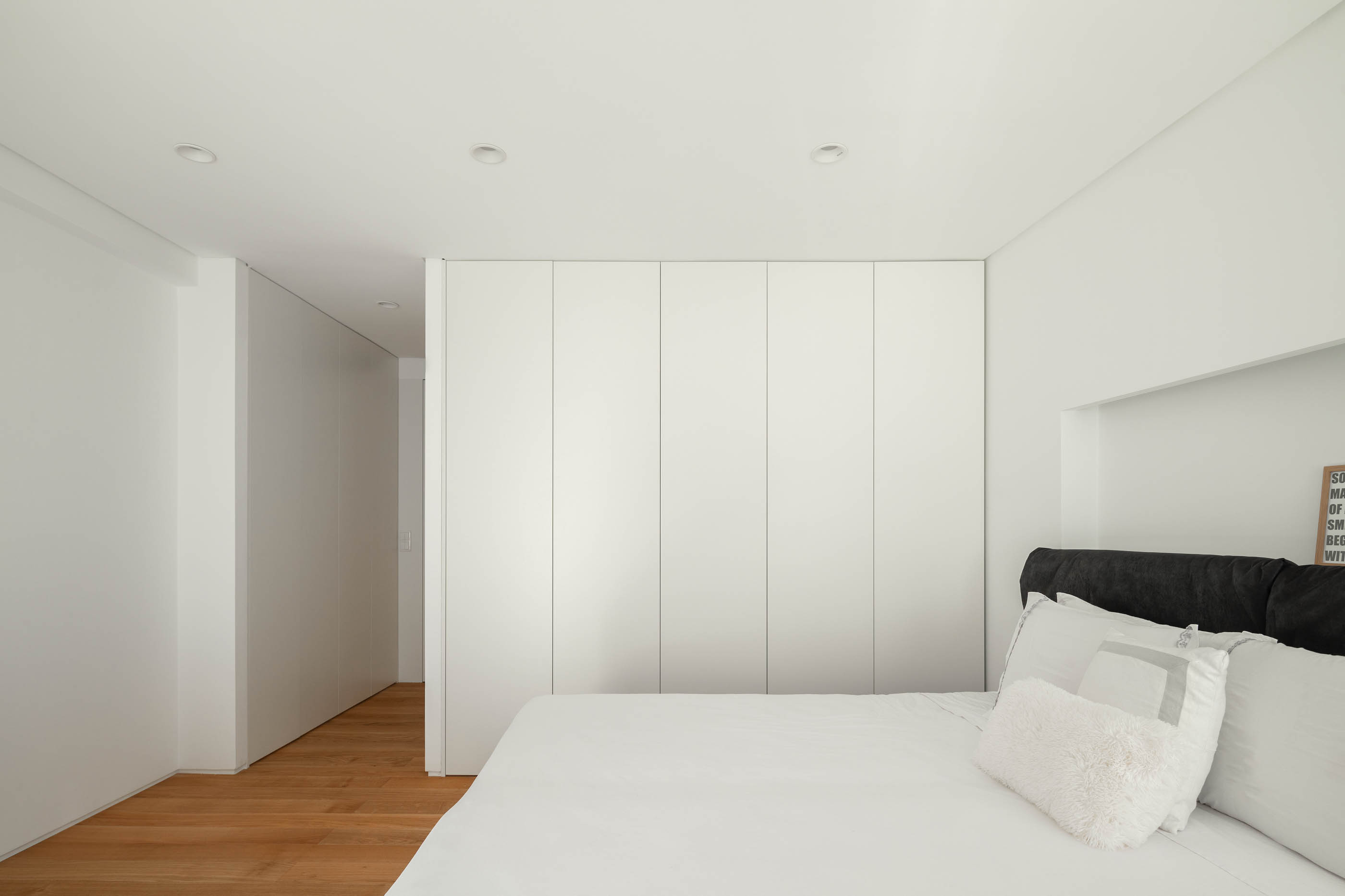 Quarto com cama branca, armário branco embutido e chão de madeira clara. — Casa GD arquitetura Esquissos Arquitectura em Portugal