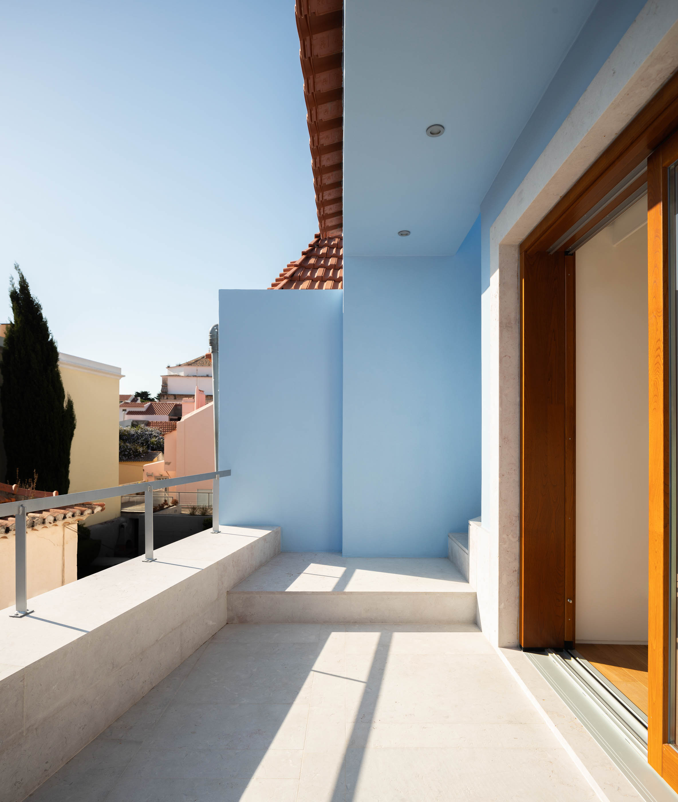 Terraço com paredes azuis, chão de pedra clara e vista para a cidade. — Casa GD arquitetura Esquissos Arquitectura em Portugal