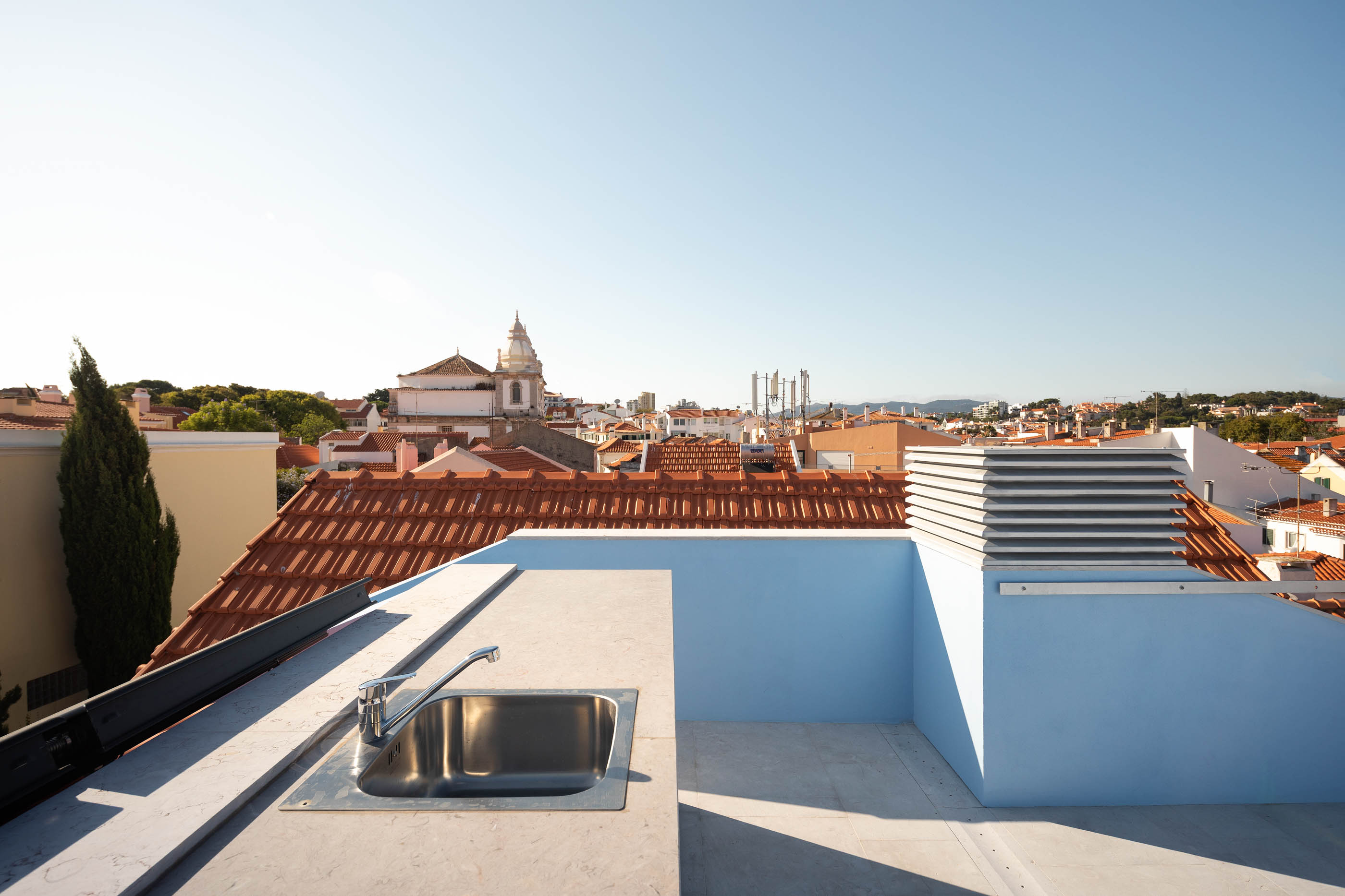 Terraço com pia de inox, paredes azuis e vista panorâmica da cidade. — Casa GD arquitetura Esquissos Arquitectura em Portugal