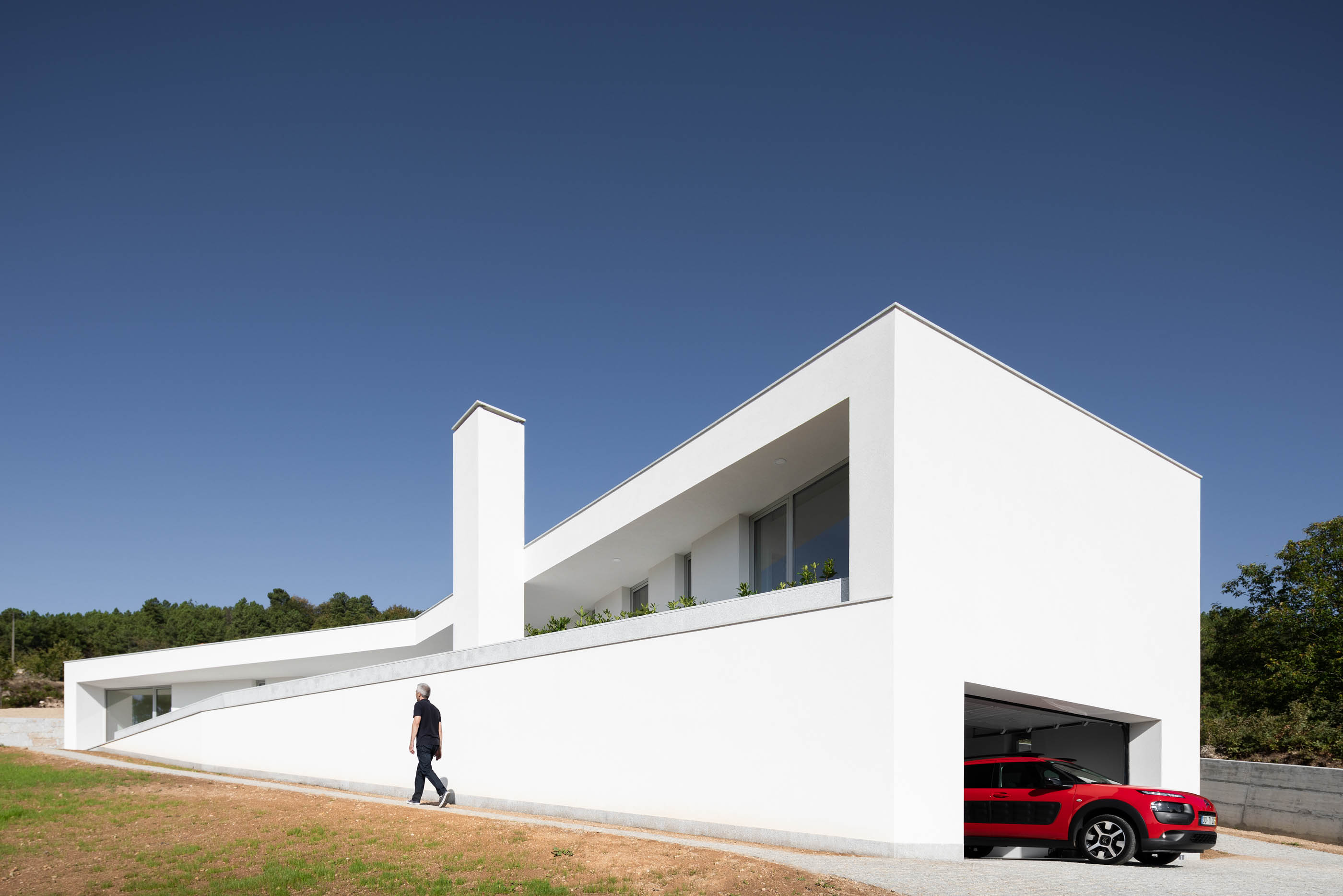 Fachada branca da moradia com garagem, rampa de acesso e um homem a caminhar. — Casa em Lamego arquitetura António Ildefonso Arquitectura em Portugal