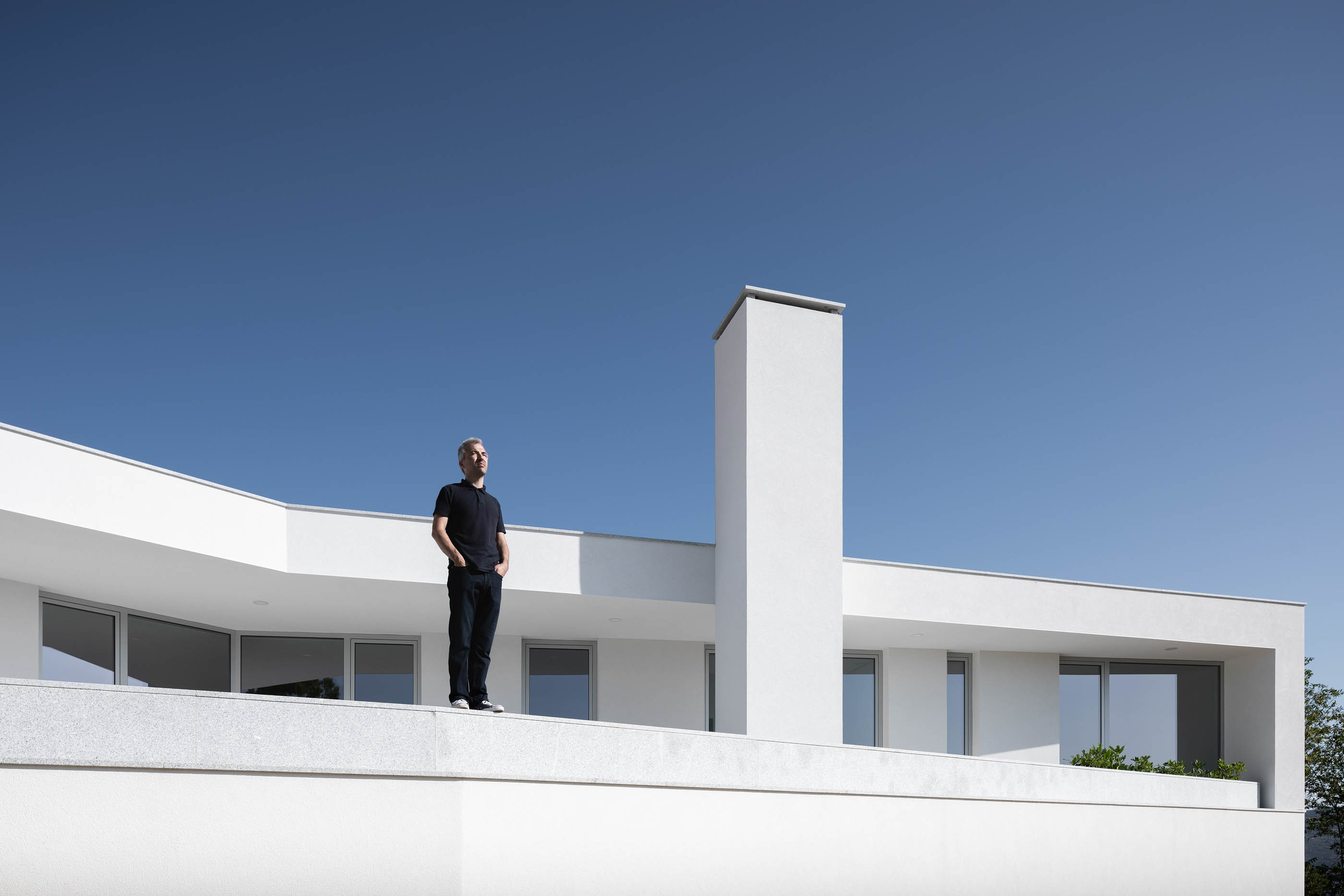 Homem em cima da casa branca, com chaminé quadrada e janelas horizontais. — Casa em Lamego arquitetura António Ildefonso Arquitectura em Portugal