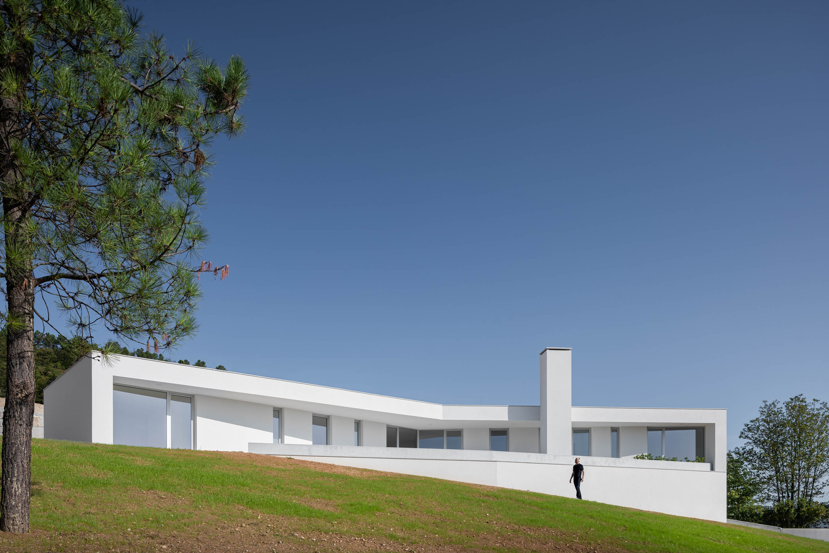 Moradia branca minimalista integrada na encosta, com amplas janelas e chaminé. — Casa em Lamego arquitetura António Ildefonso Arquitectura em Portugal