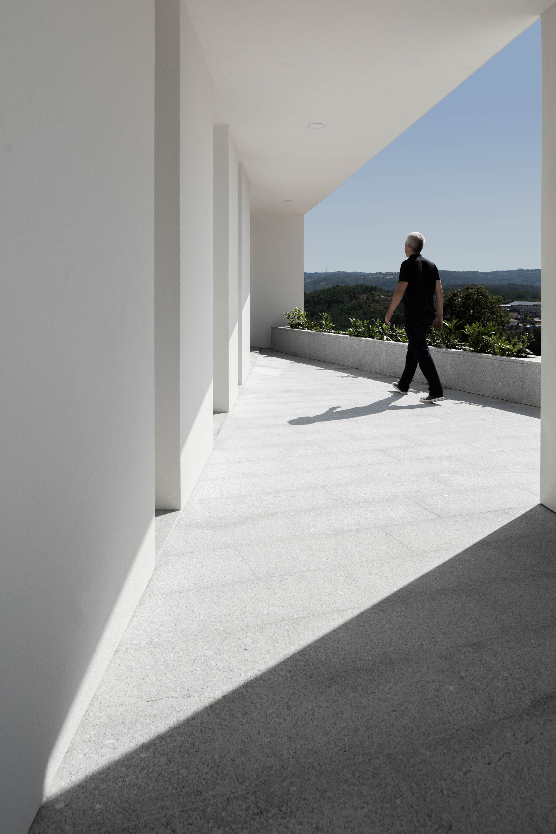 Homem a caminhar num corredor exterior branco, com vista para a paisagem. — Casa em Lamego arquitetura António Ildefonso Arquitectura em Portugal