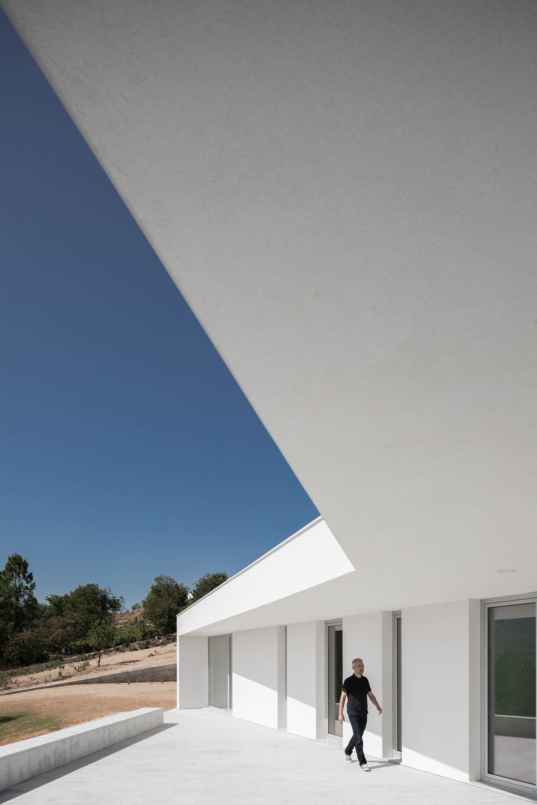 Detalhe da arquitetura branca minimalista, com homem a caminhar no terraço. — Casa em Lamego arquitetura António Ildefonso Arquitectura em Portugal
