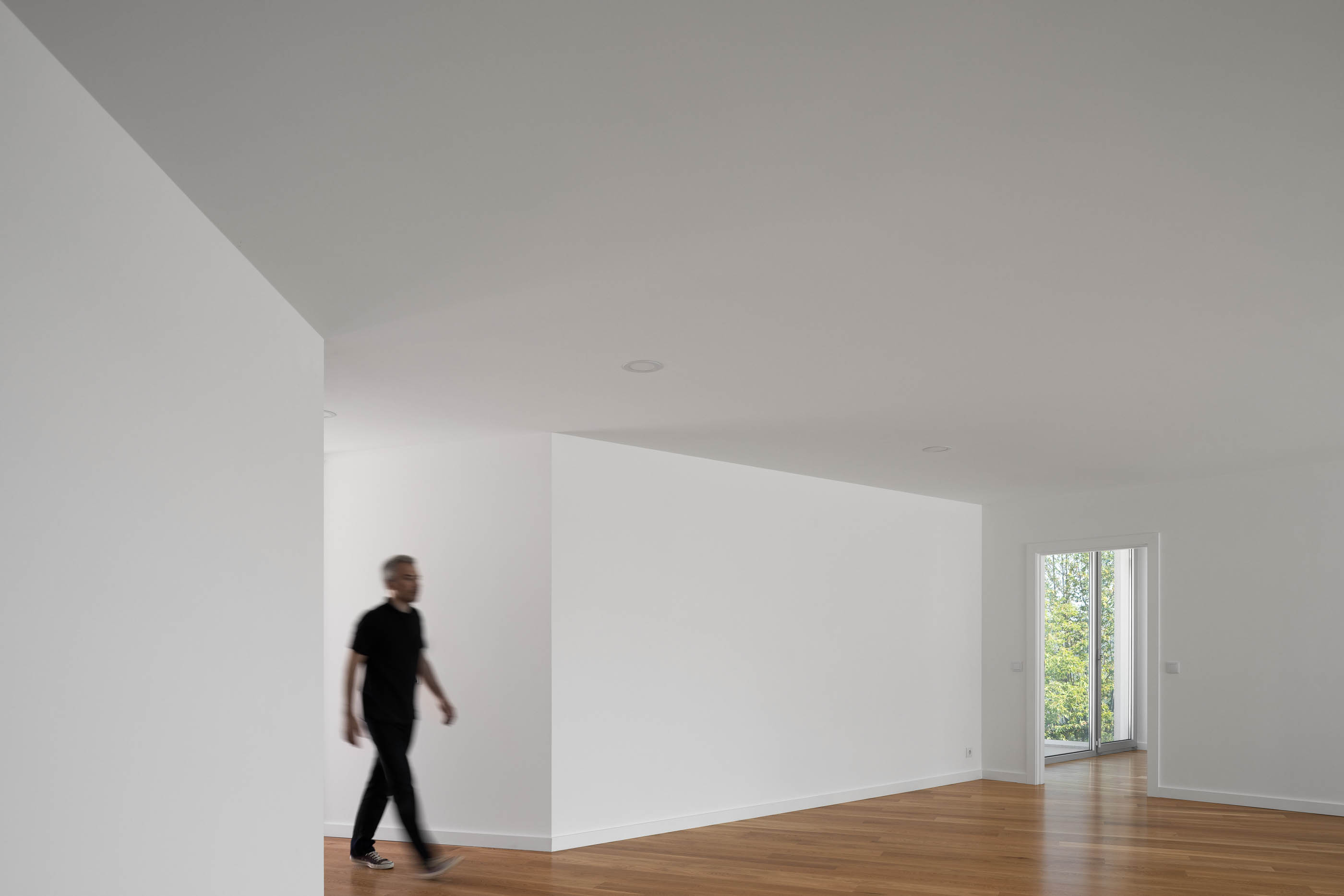 Interior da casa com paredes brancas, chão de madeira e homem a caminhar. — Casa em Lamego arquitetura António Ildefonso Arquitectura em Portugal