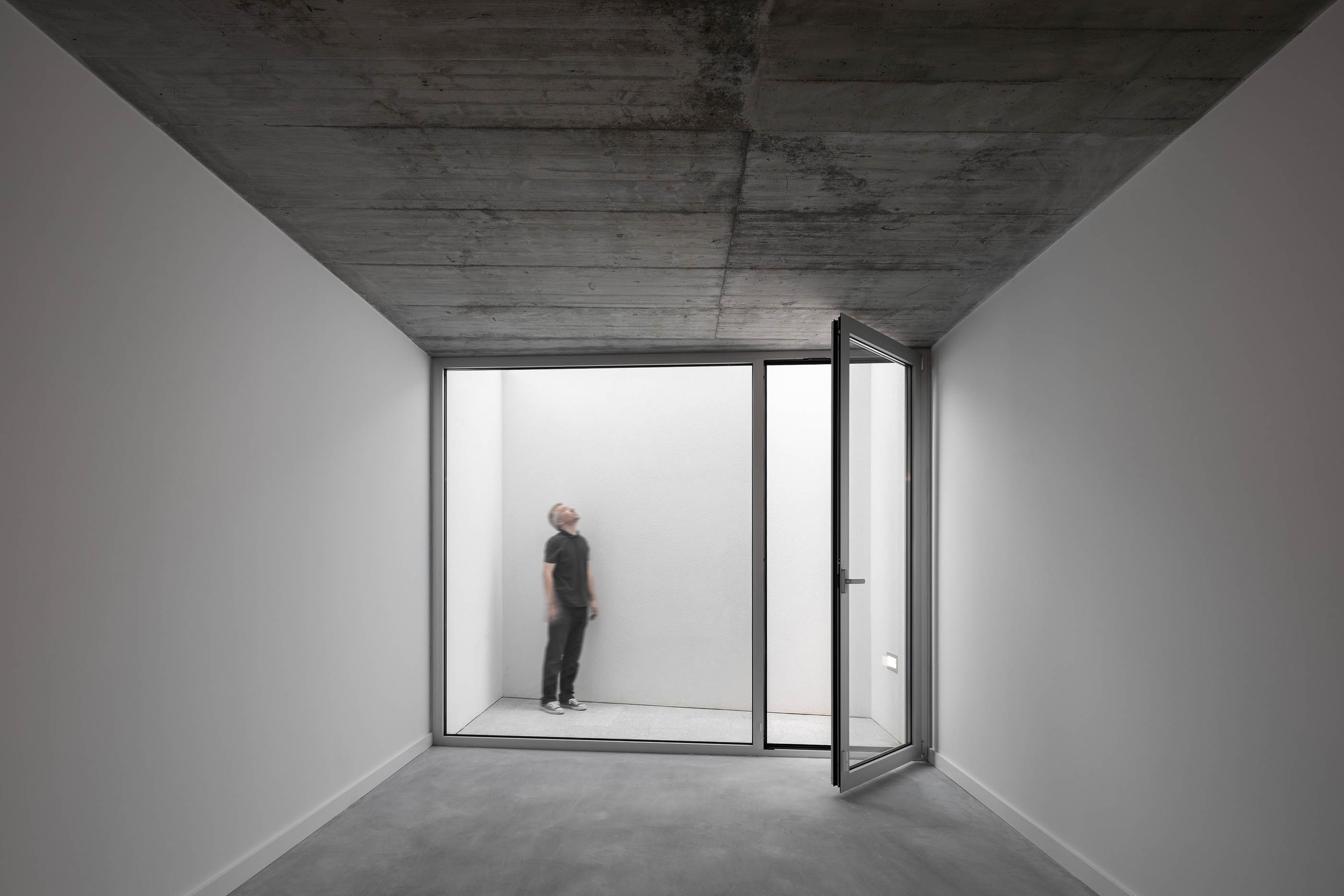 Pequeno pátio interior com paredes brancas, chão de cimento e teto de betão. — Casa em Lamego arquitetura António Ildefonso Arquitectura em Portugal