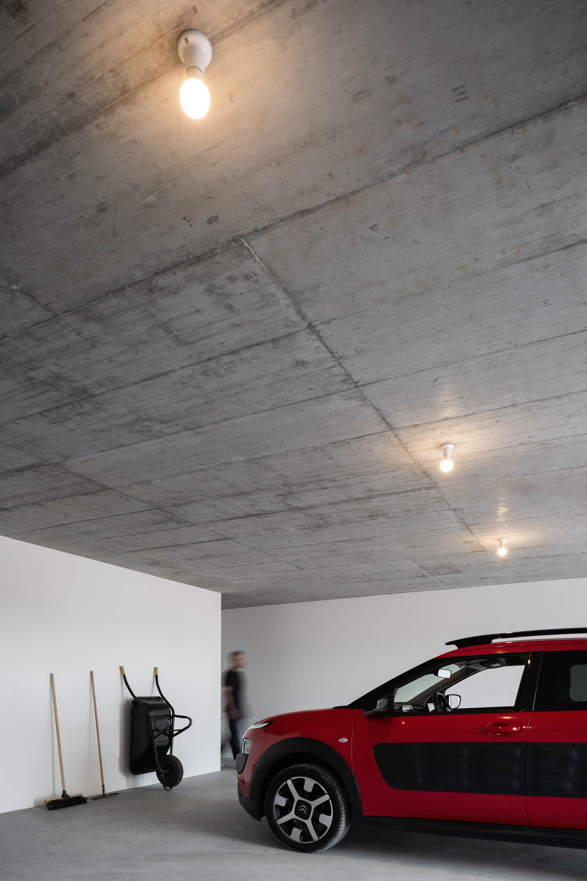 Garagem com teto de betão aparente, carro vermelho e iluminação simples. — Casa em Lamego arquitetura António Ildefonso Arquitectura em Portugal