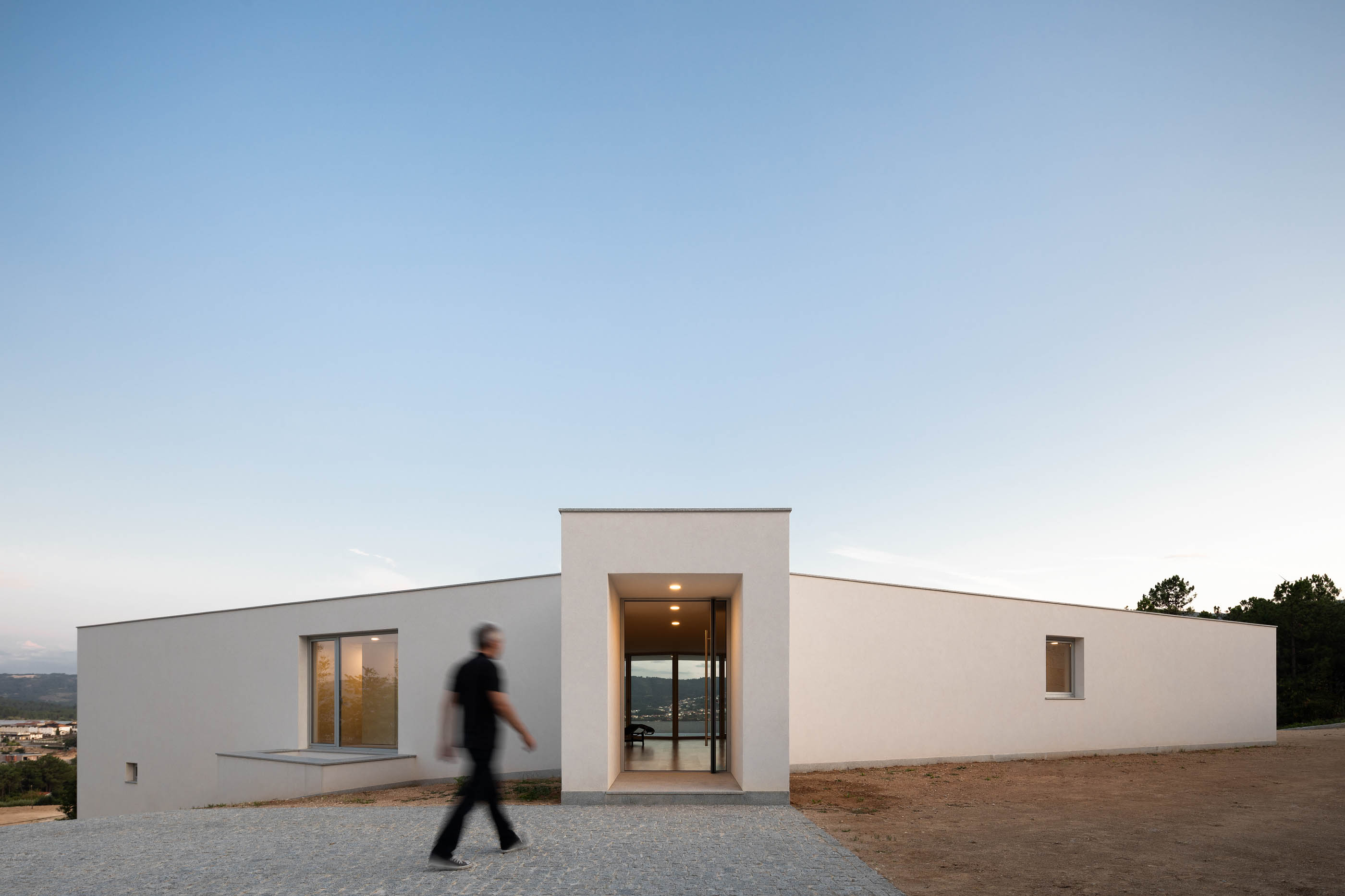 Fachada frontal da casa branca ao entardecer, com homem a caminhar. — Casa em Lamego arquitetura António Ildefonso Arquitectura em Portugal