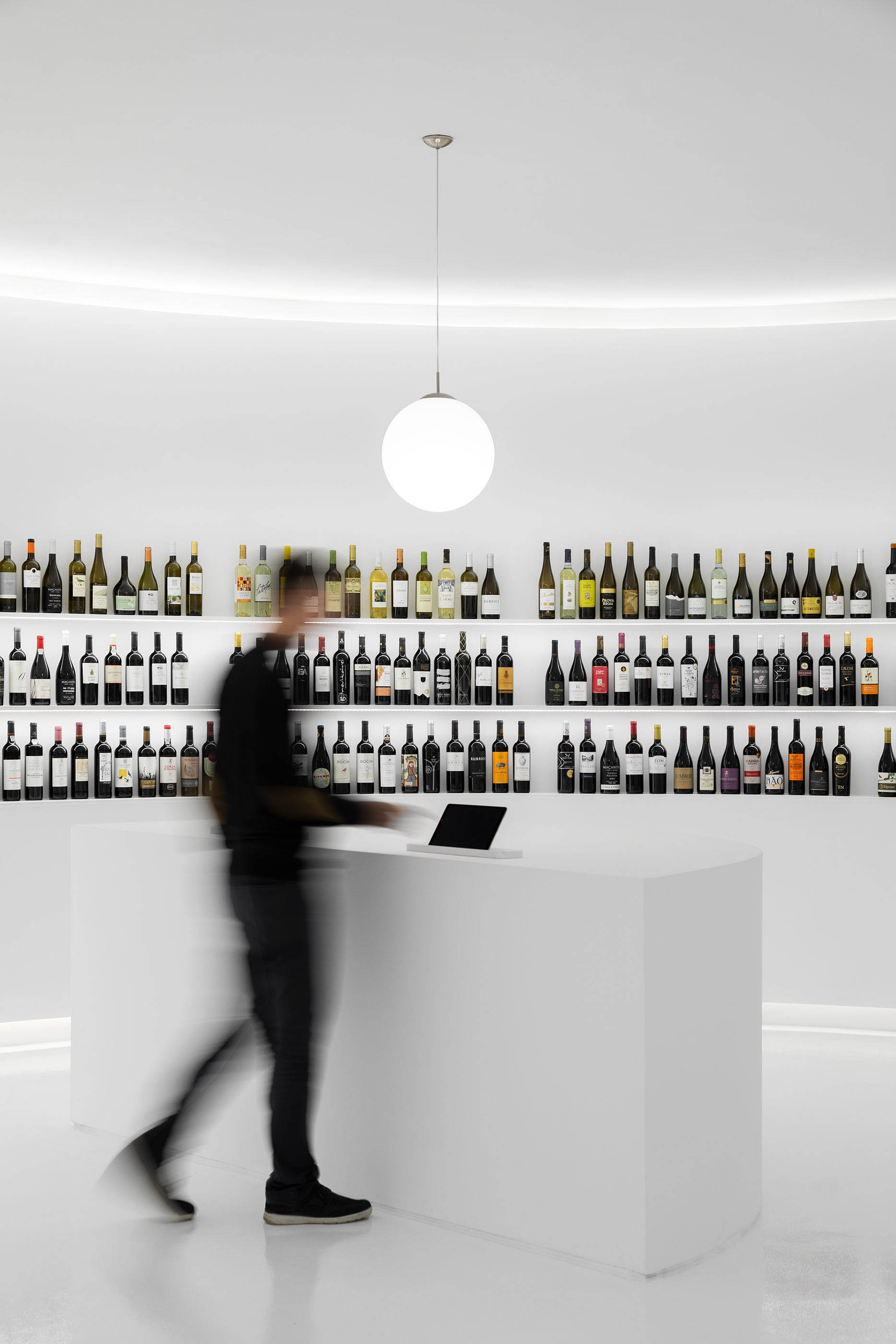 Balcão curvo branco minimalista com garrafas de vinho expostas e iluminação esférica suspensa. — Portugal Vineyards Concept Store arquitetura Porto Architects em Porto