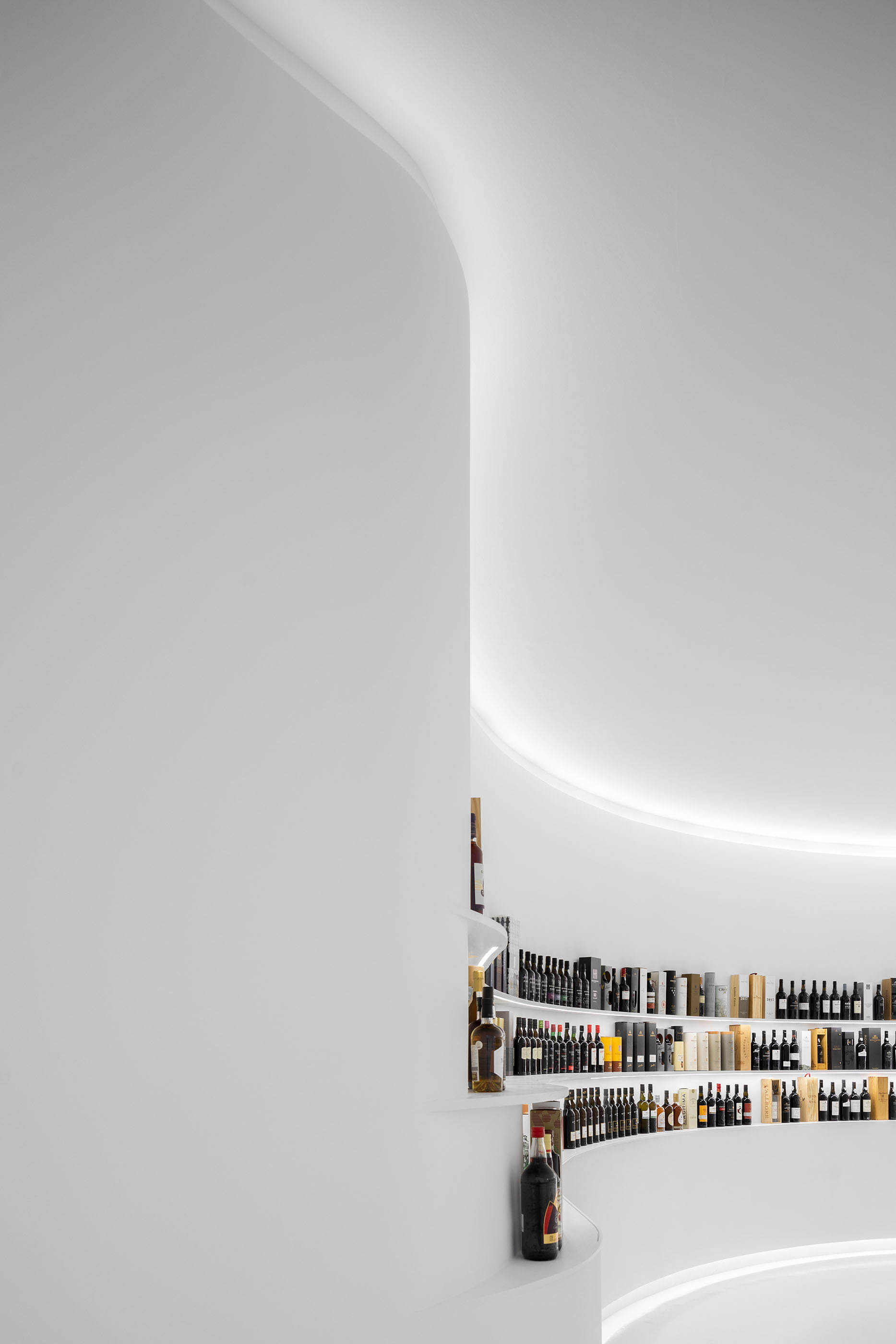 Detalhe da parede curva com prateleiras de vinho iluminadas, estilo minimalista e cor branca predominante. — Portugal Vineyards Concept Store arquitetura Porto Architects em Porto