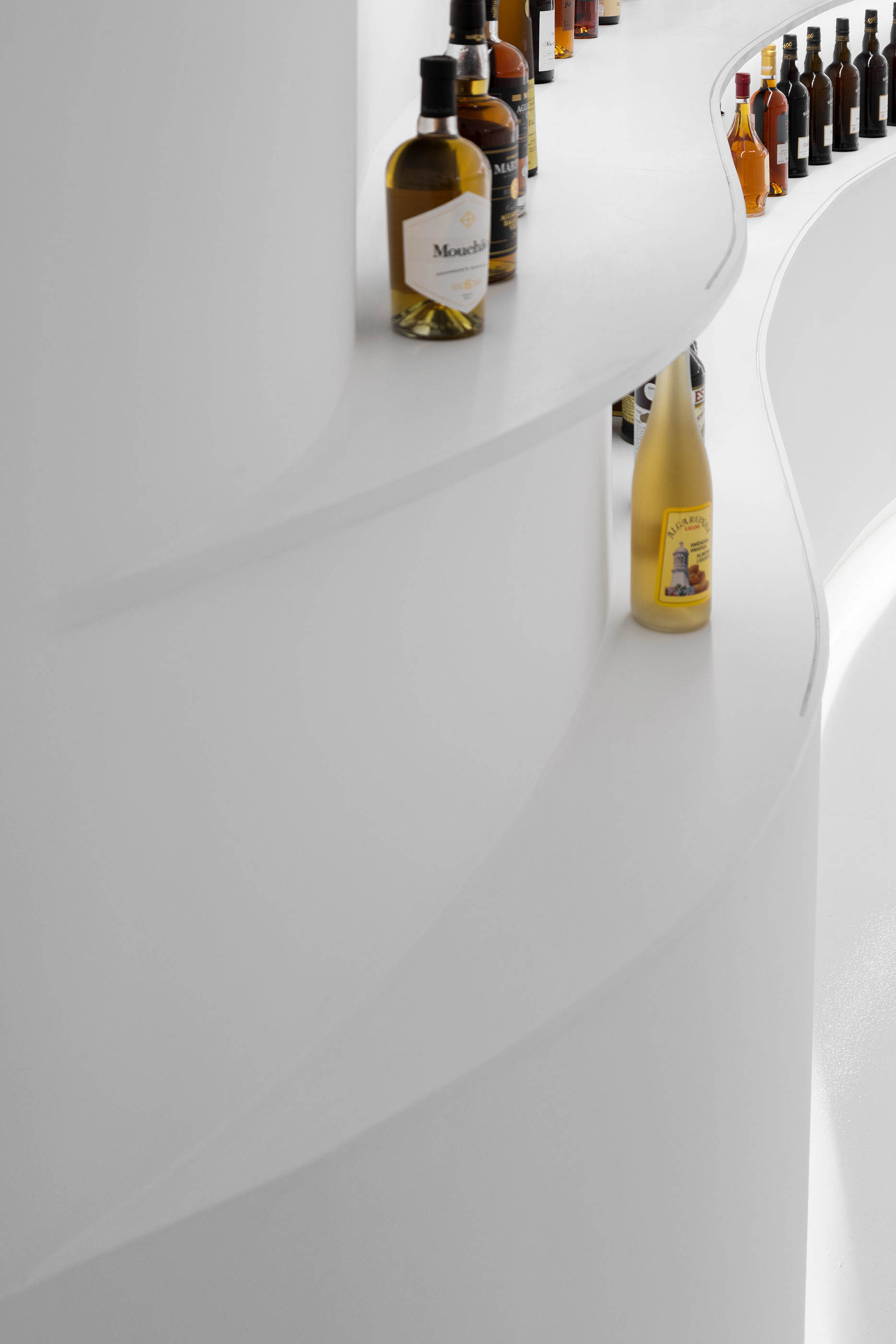 Detalhe das prateleiras curvas com garrafas de vinho, mostrando a continuidade do design e a iluminação linear. — Portugal Vineyards Concept Store arquitetura Porto Architects em Porto