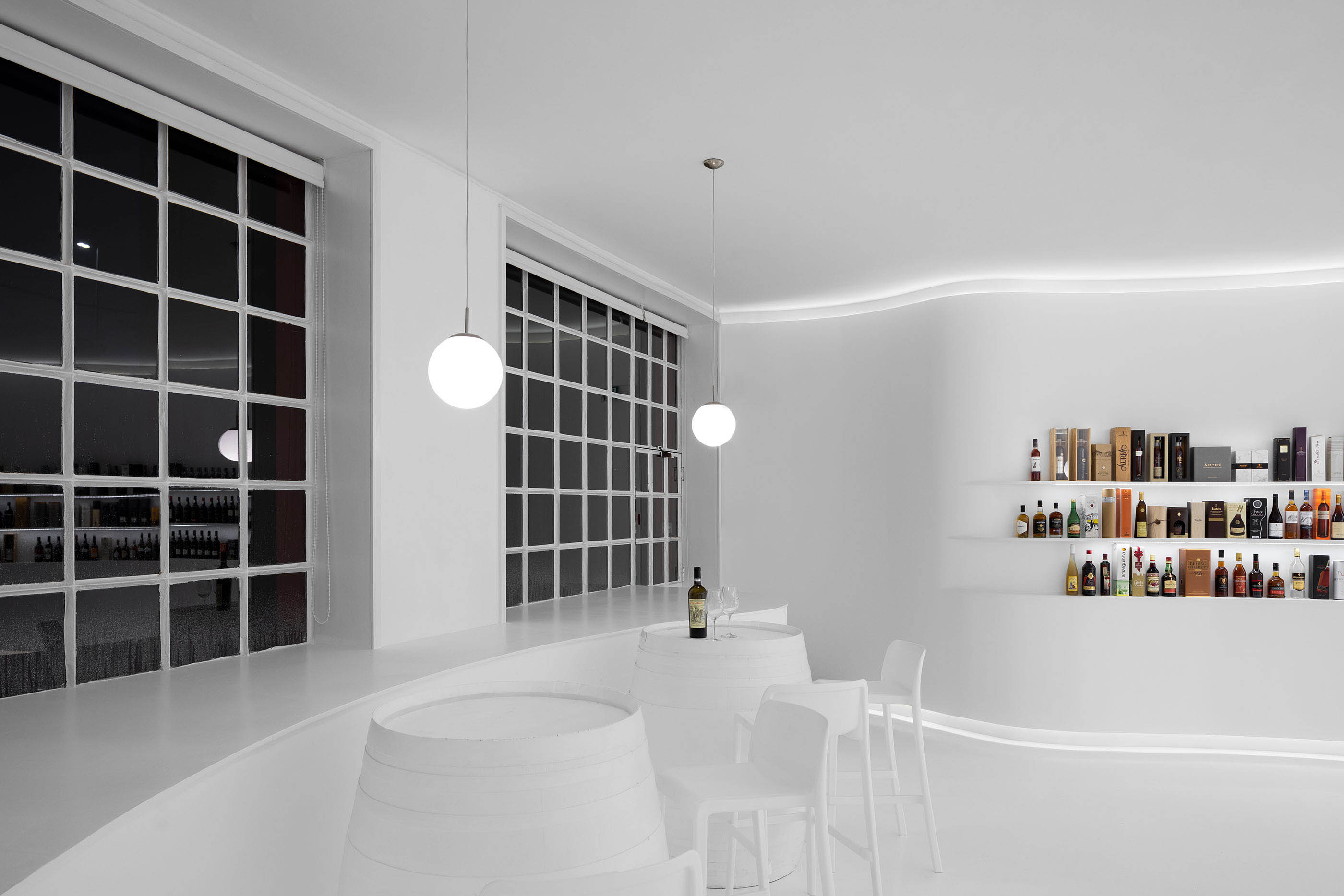Área de degustação com barris transformados em mesas, cadeiras brancas e janelas amplas, ambiente luminoso. — Portugal Vineyards Concept Store arquitetura Porto Architects em Porto