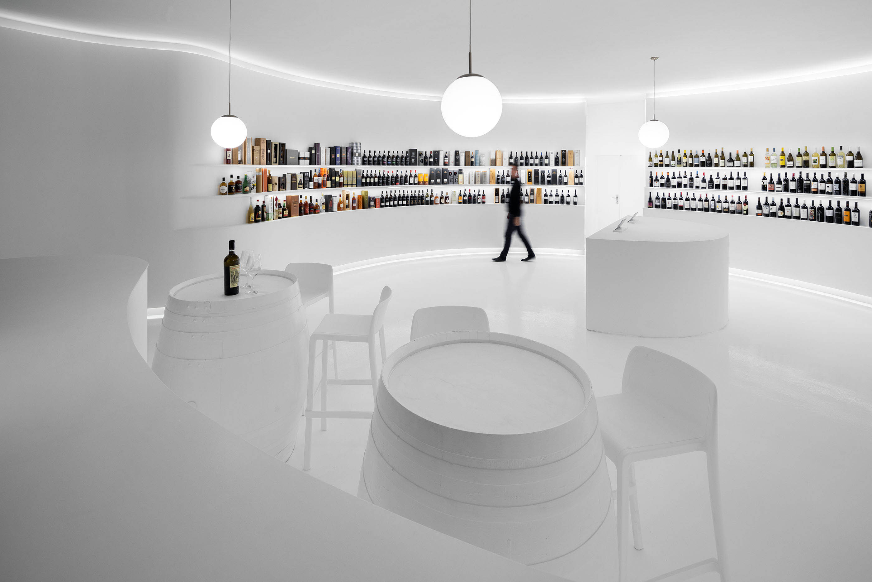 Visão geral do espaço com área de degustação, balcão e prateleiras de vinho, design curvo e minimalista. — Portugal Vineyards Concept Store arquitetura Porto Architects em Porto