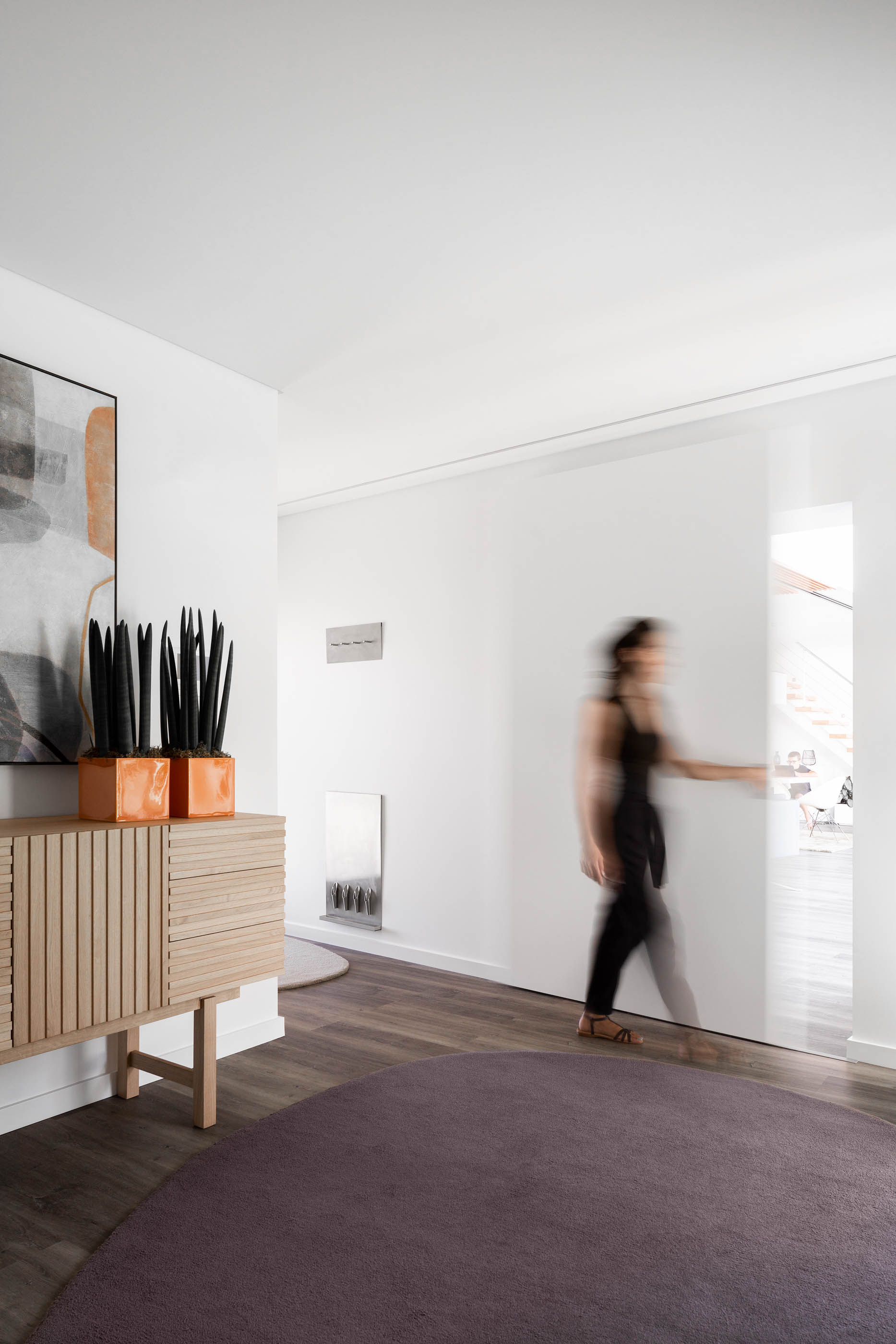 Hall de entrada com aparador em madeira ripada, tapete redondo roxo e obra de arte moderna na parede. — Reabilitação Casa J arquitetura Frari em Portugal