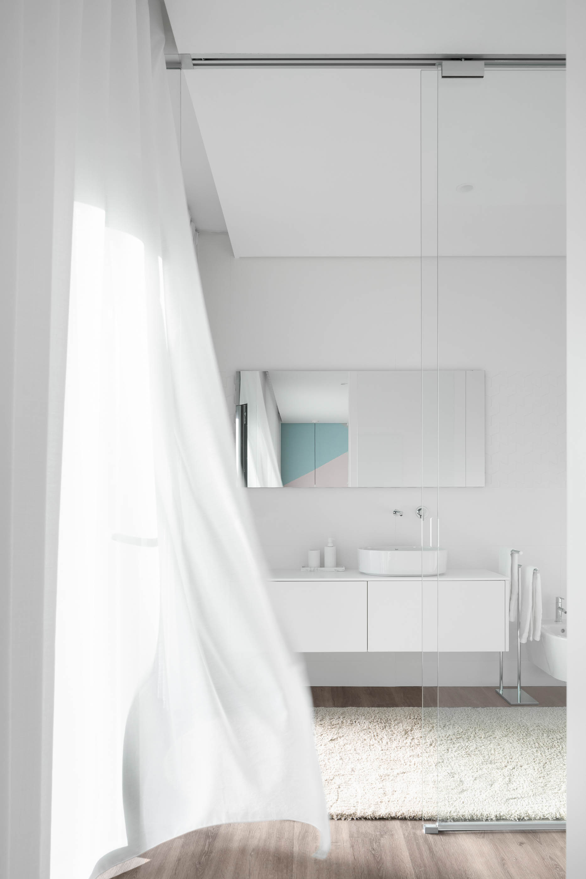 Casa de banho luminosa com cortina branca, lavatório redondo sobre móvel branco e espelho retangular. — Reabilitação Casa J arquitetura Frari em Portugal